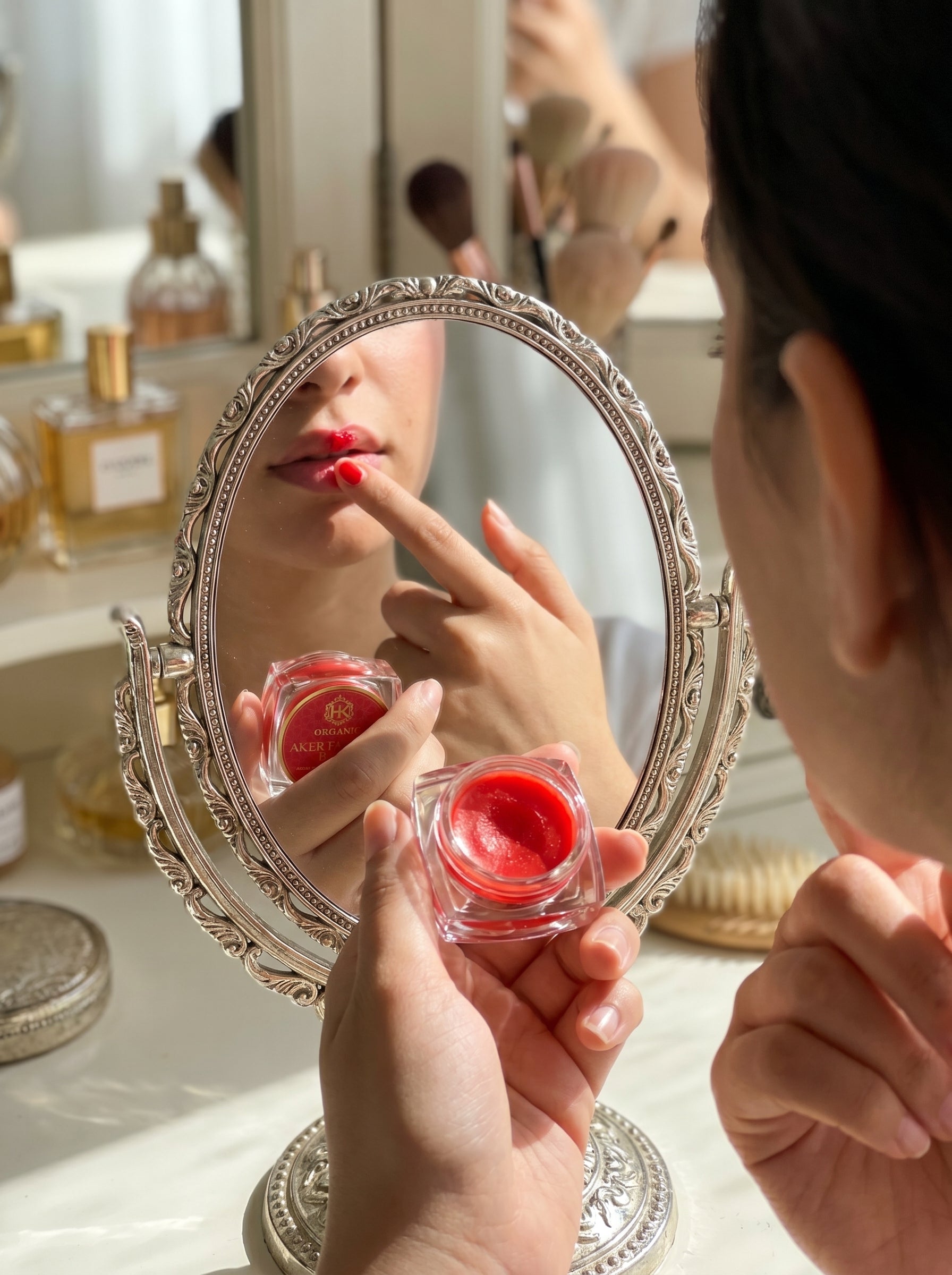 Person applying red lipstick in front of a mirror with beauty products in the background