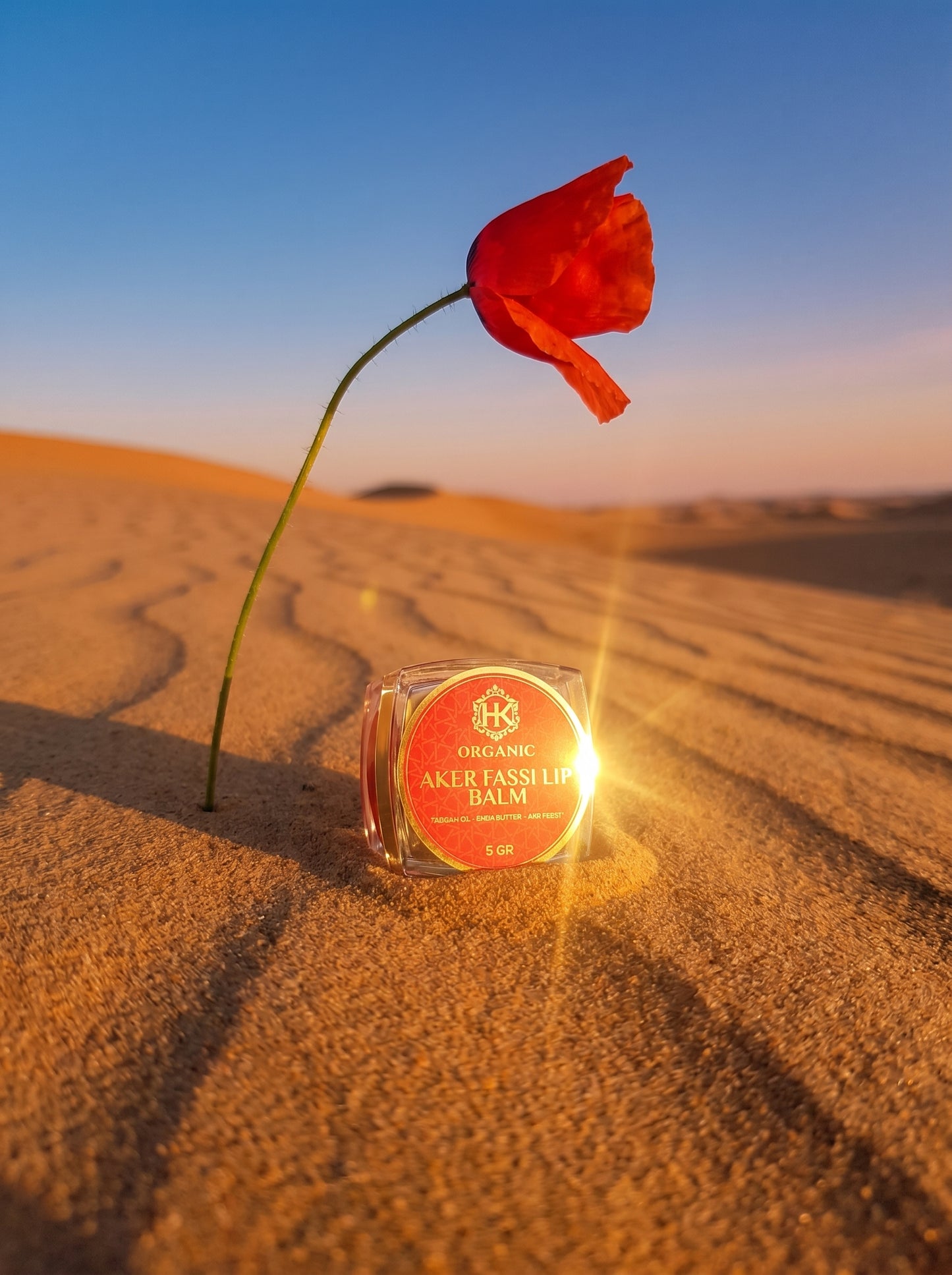 Red flower and jar of balm on sand with sunset sky