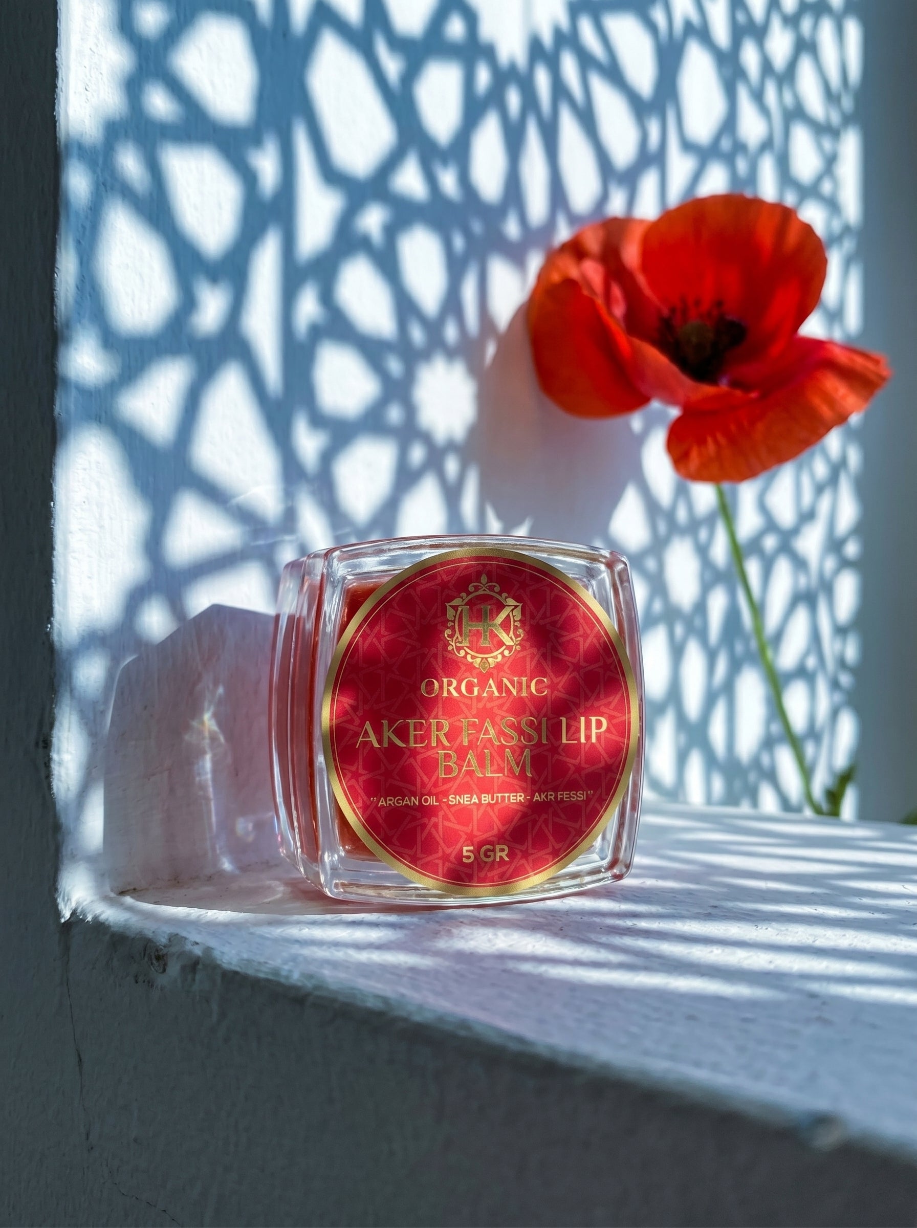 Lip balm with red label on a white surface with a red flower in the background