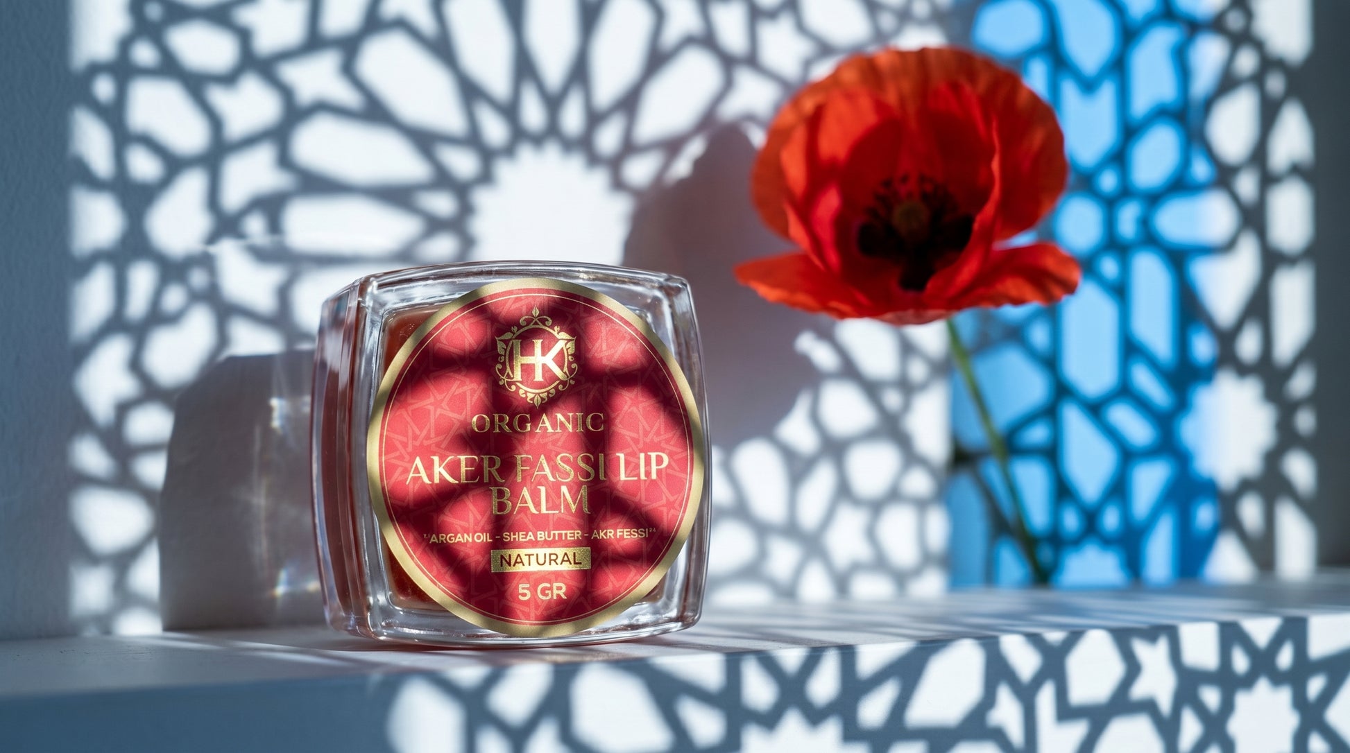 Lip balm with red label on a white surface with a red flower in the background