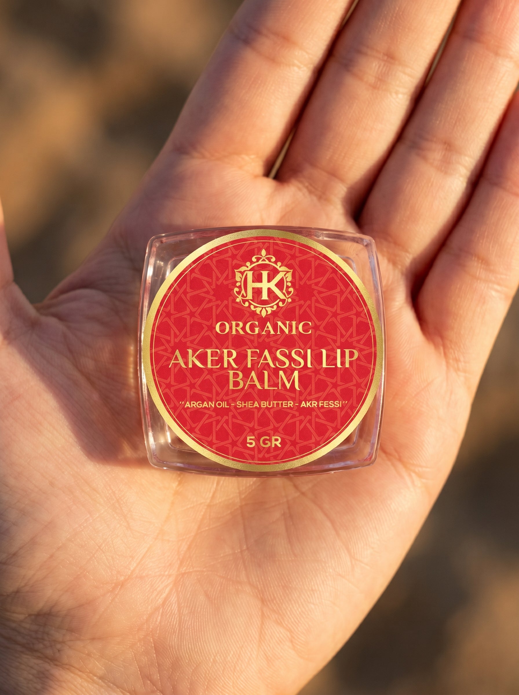 Lip balm container labeled 'Aker Fassil' held in a hand with a blurred background