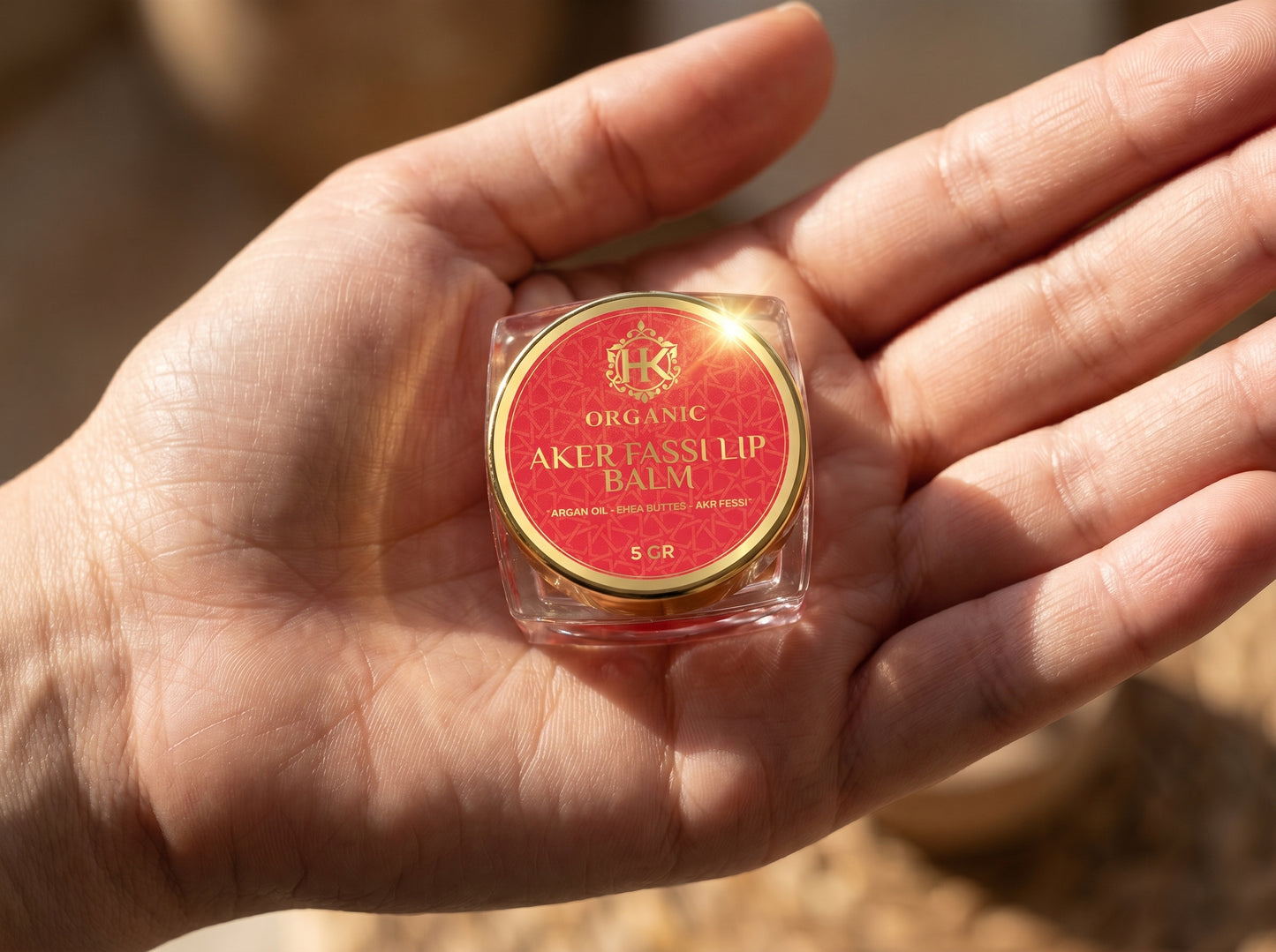Hand holding a small container of Organic Aker Tassil lip balm with a red label.