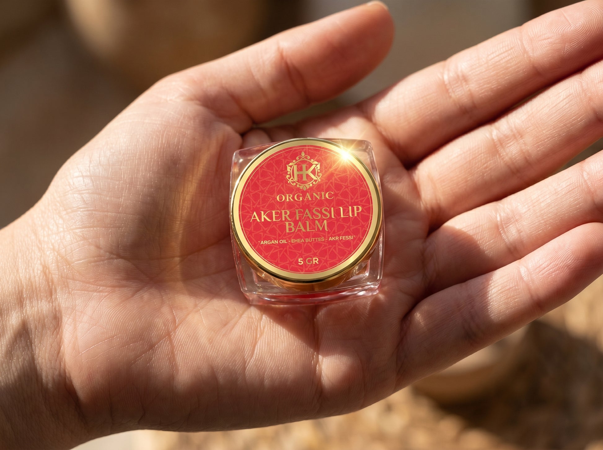 Hand holding a small container of Organic Aker Tassil lip balm with a red label.