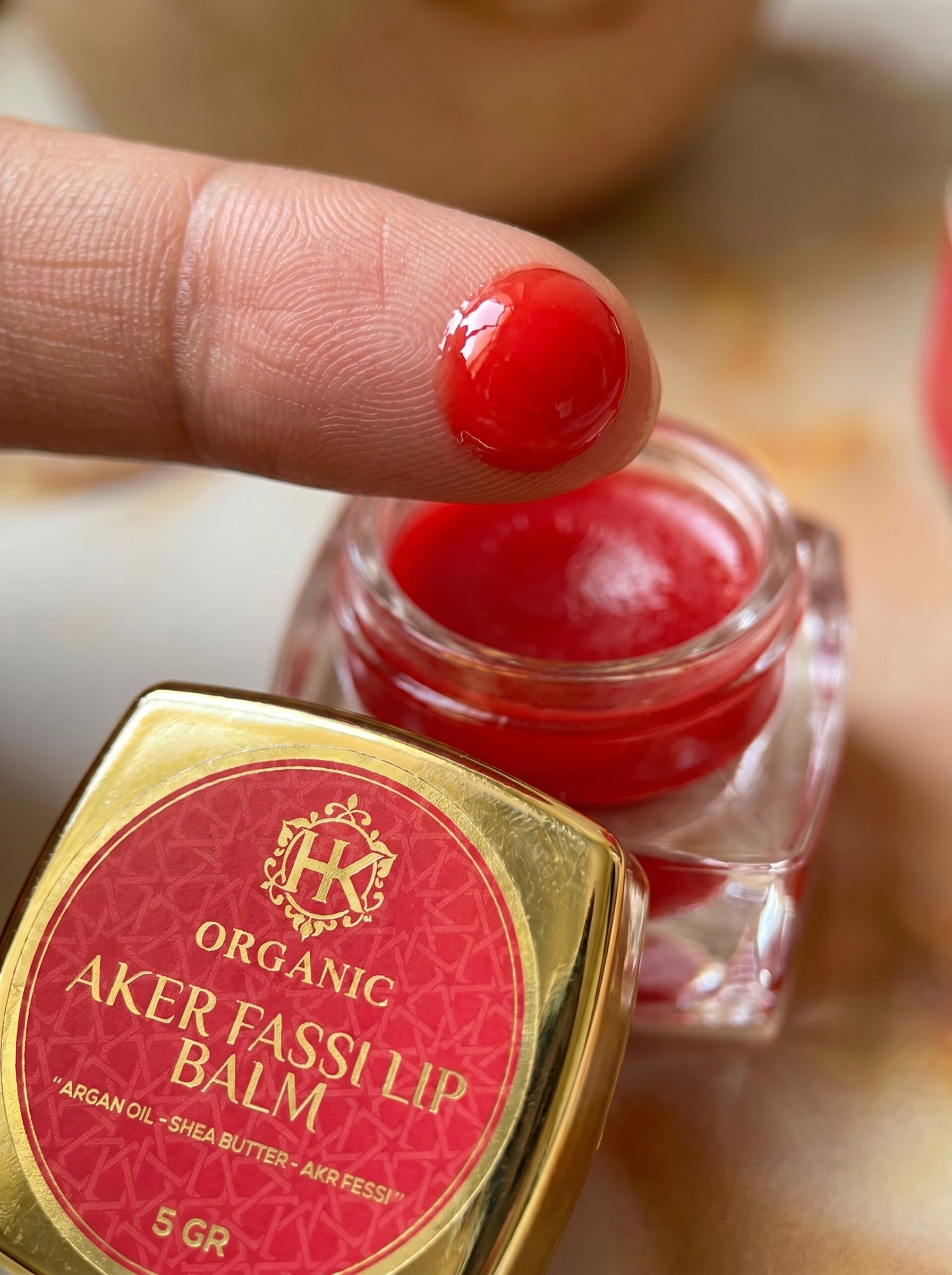 Organic Aker Fassi lip balm with a red substance on a finger, brand logo visible