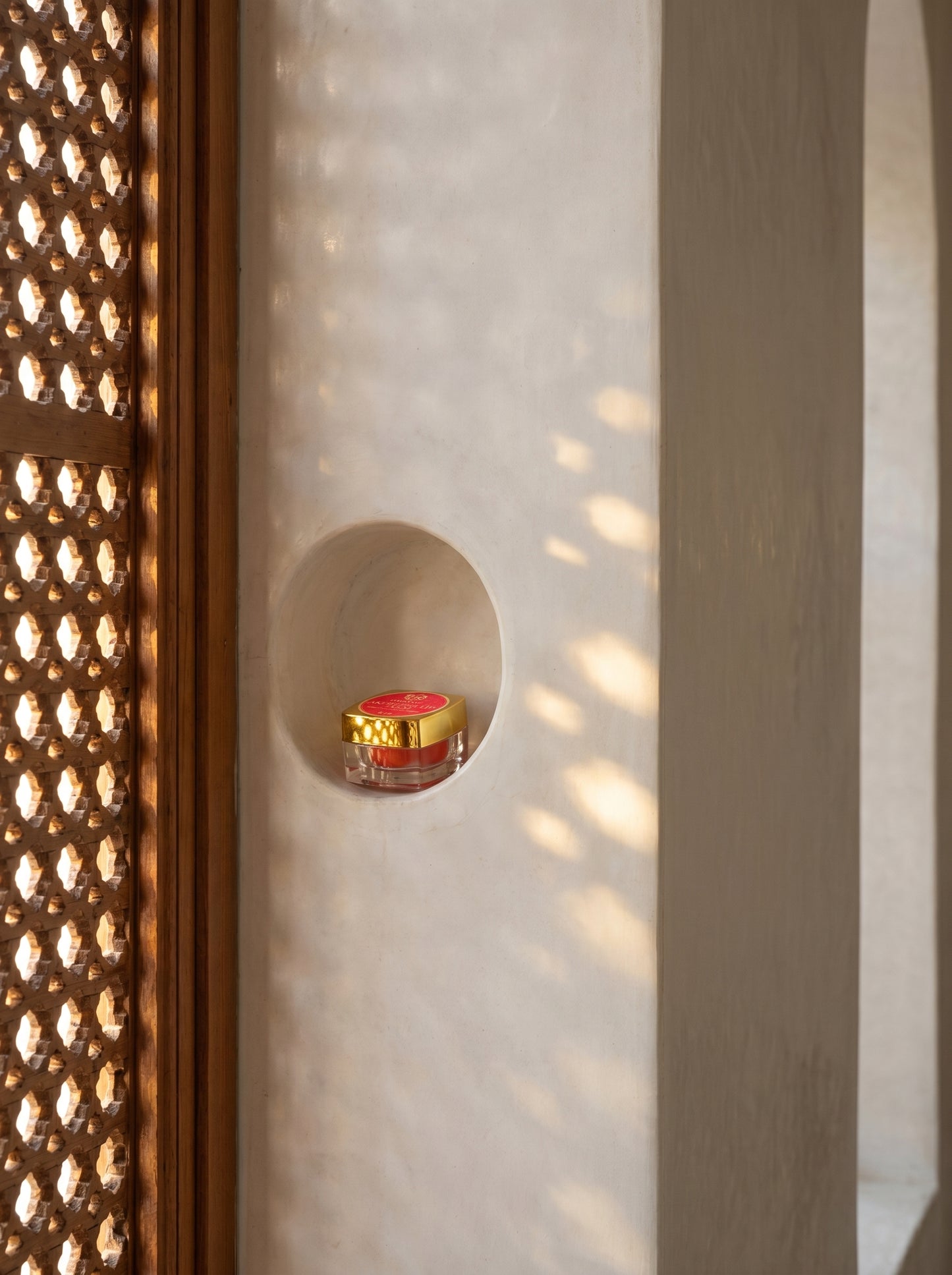 Small red candle in a decorative holder against a textured wall with geometric patterns.