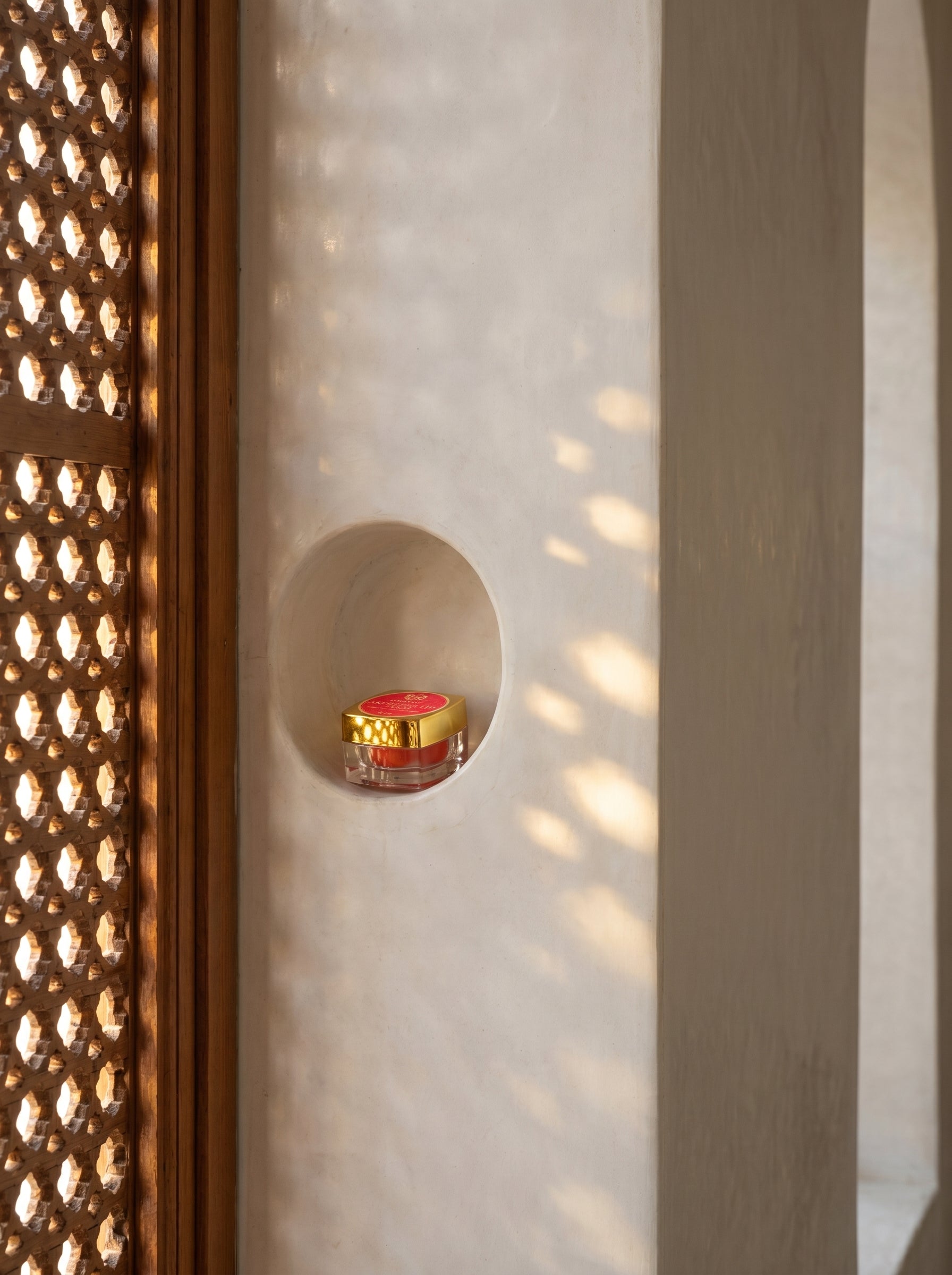 Small red candle in a decorative holder against a textured wall with geometric patterns.