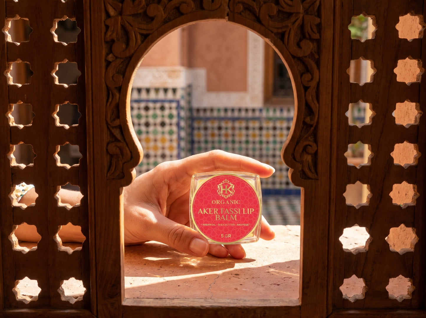 Hand holding a lip balm in front of a decorative mirror with a colorful background