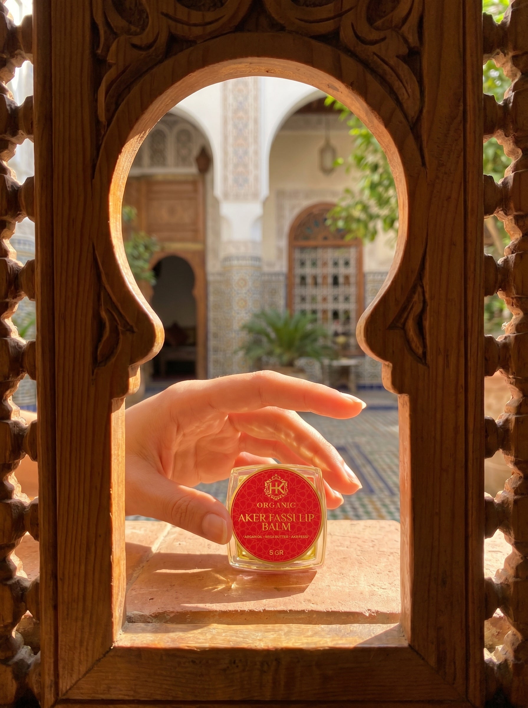 Hand holding a small bottle labeled 'Rafael' through an ornate wooden frame with a blurred outdoor background.