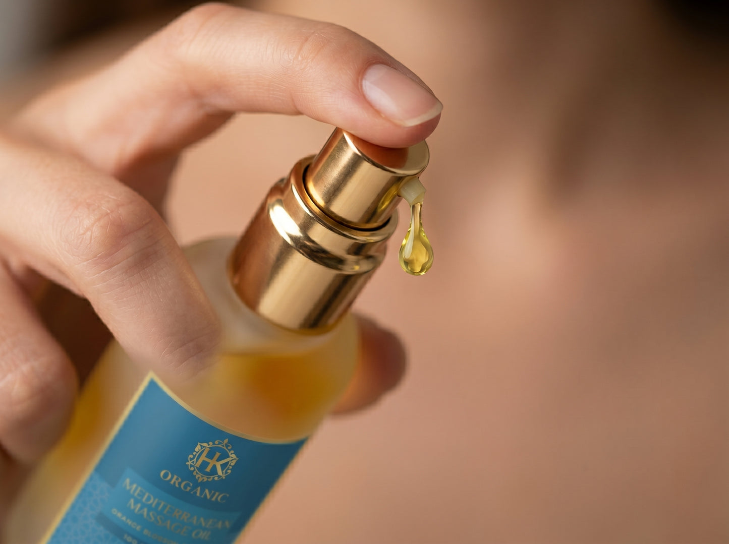 Hand holding a bottle of organic mediterranean hair oil with a droplet on a blurred background
