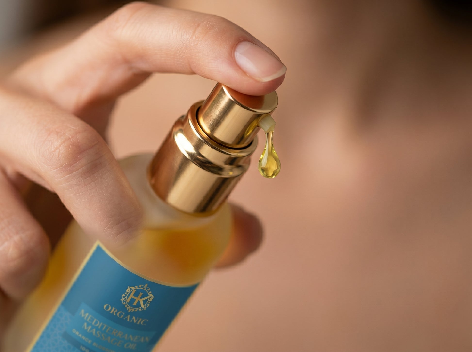 Hand holding a bottle of organic mediterranean hair oil with a droplet on a blurred background