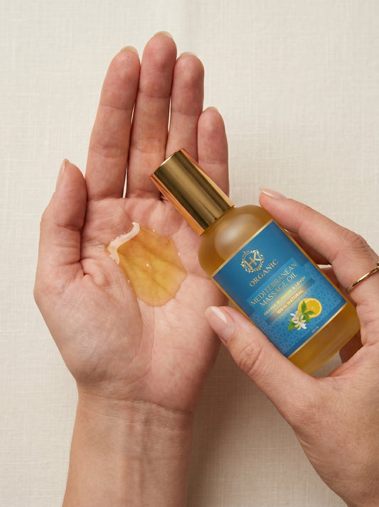 Hand holding a bottle of olive oil with a droplet on another hand against a neutral background