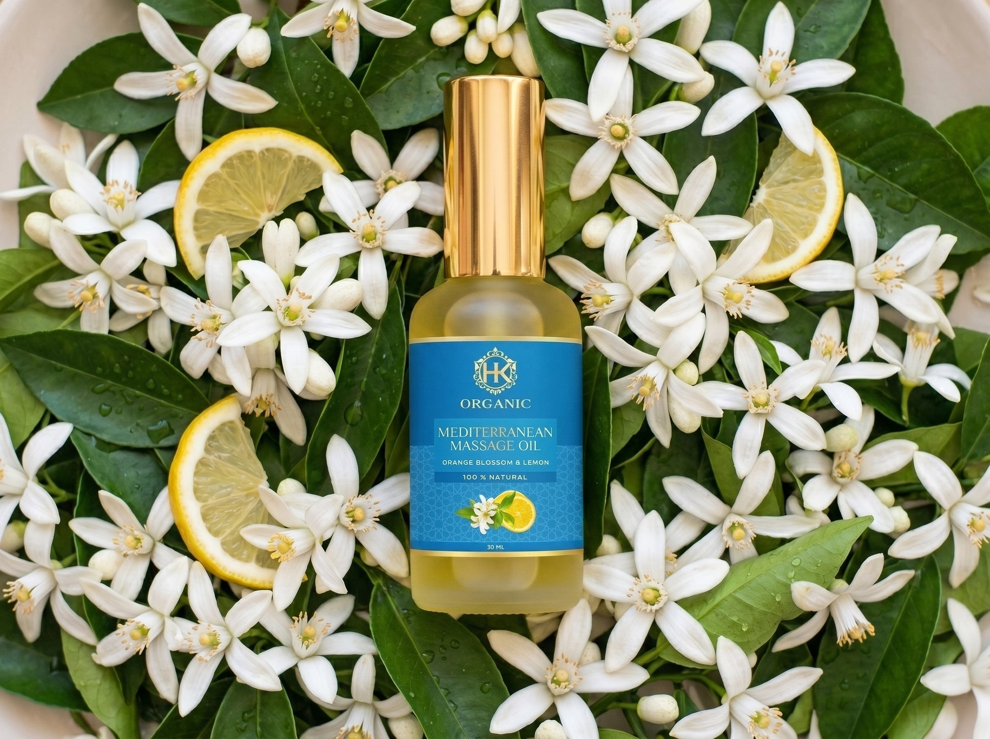 Bottle of Mediterranean Manzanilla organic oil surrounded by white flowers and lemon slices on a white background