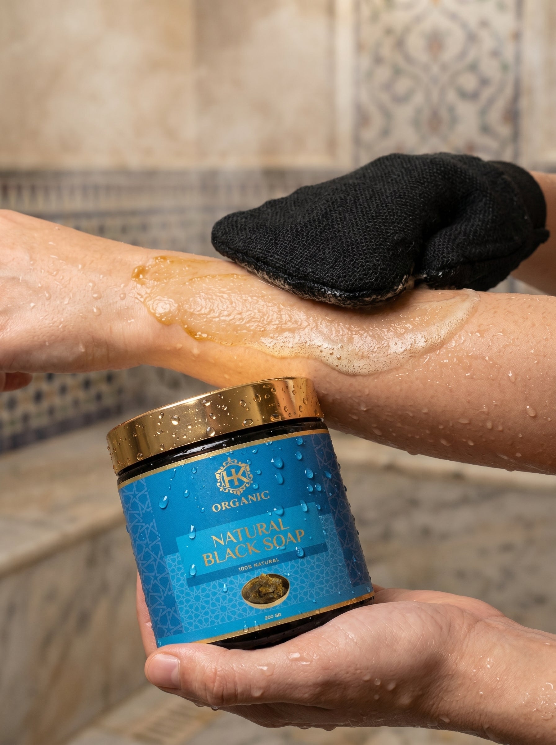 Person using natural black soap on their arm with a jar of soap in the foreground.
