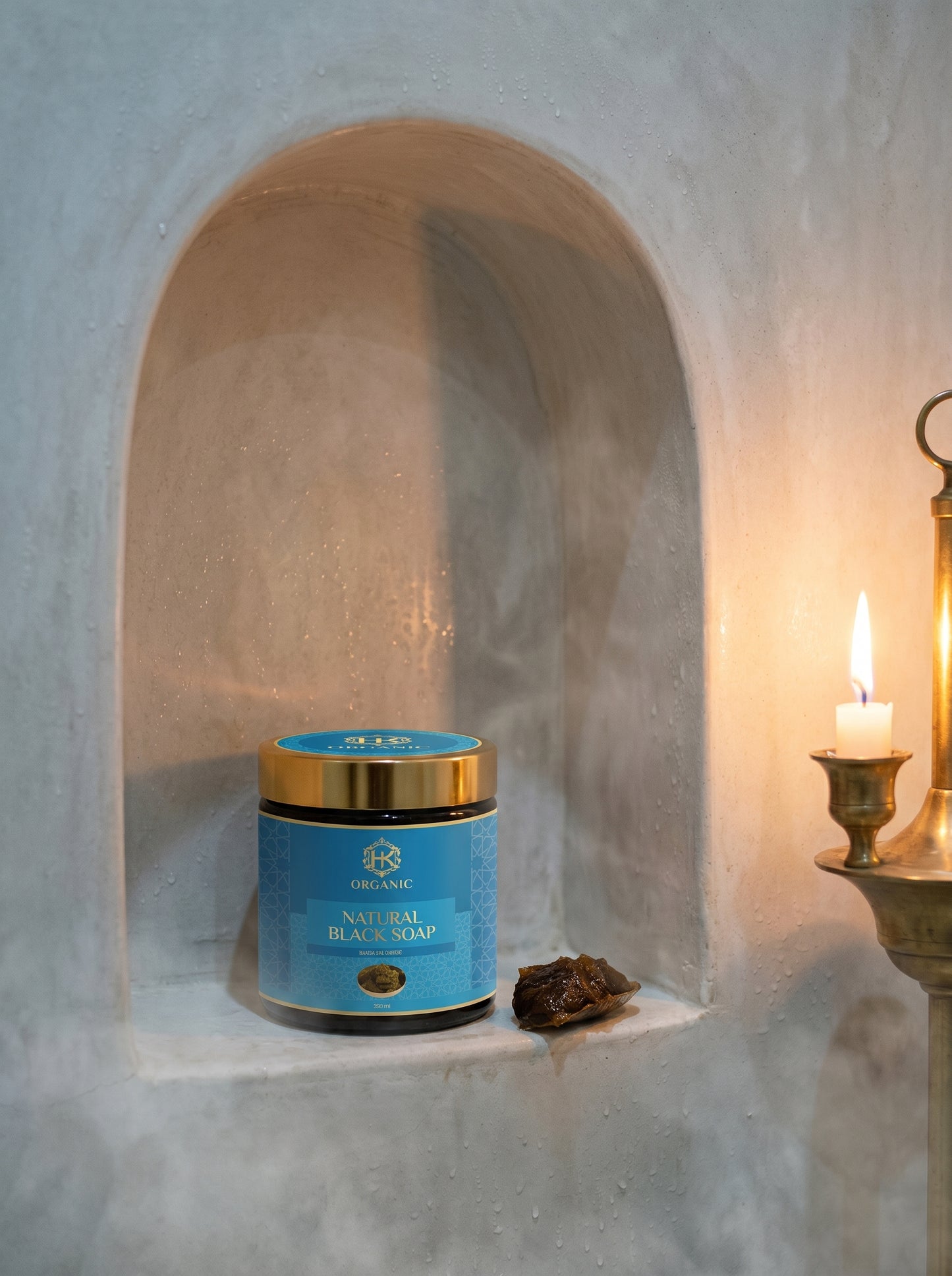 Blue jar with gold lid on a stone shelf against a textured wall with a candle.