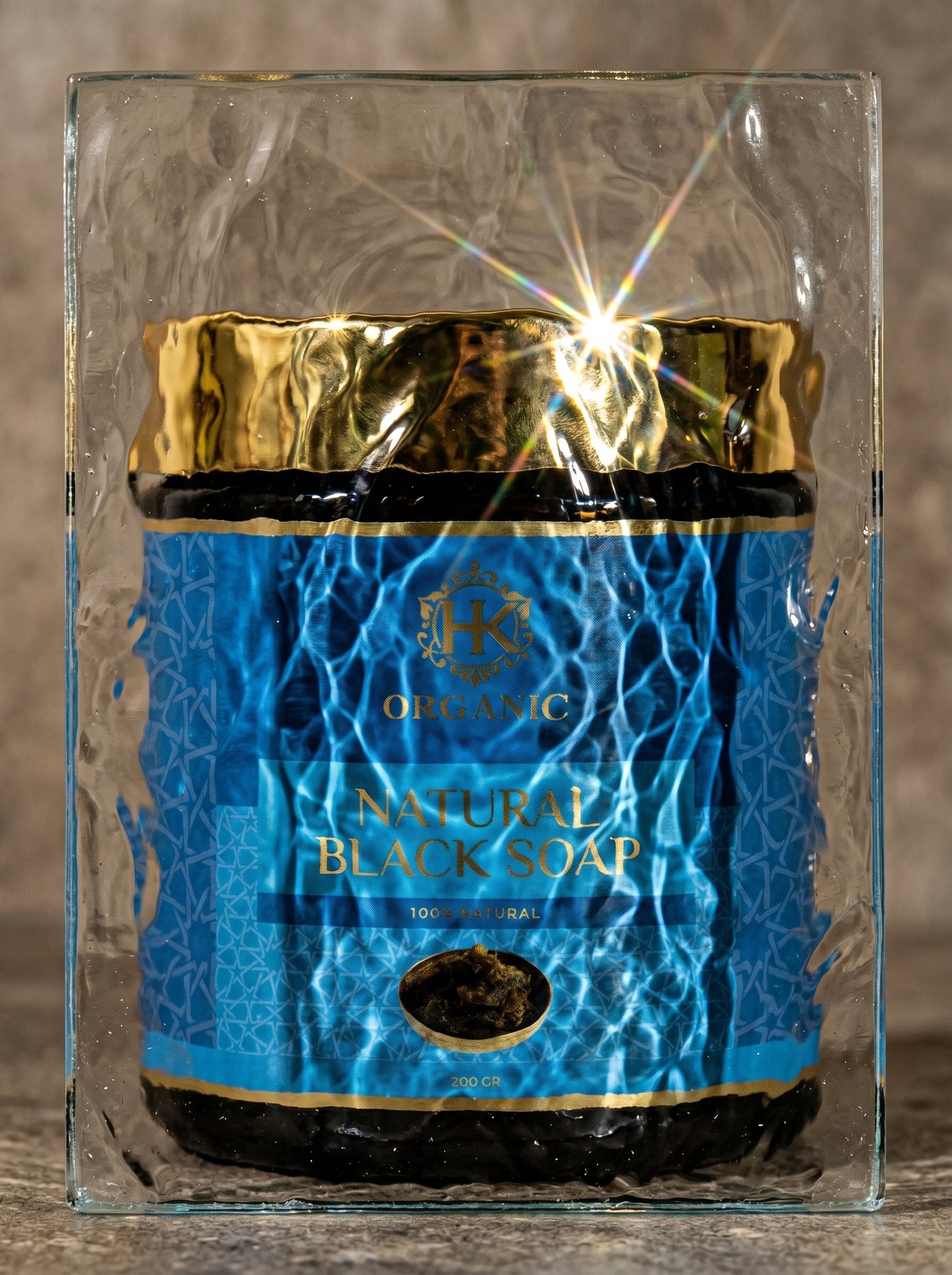 Jar of natural black soap with blue label and gold accents on a reflective surface.