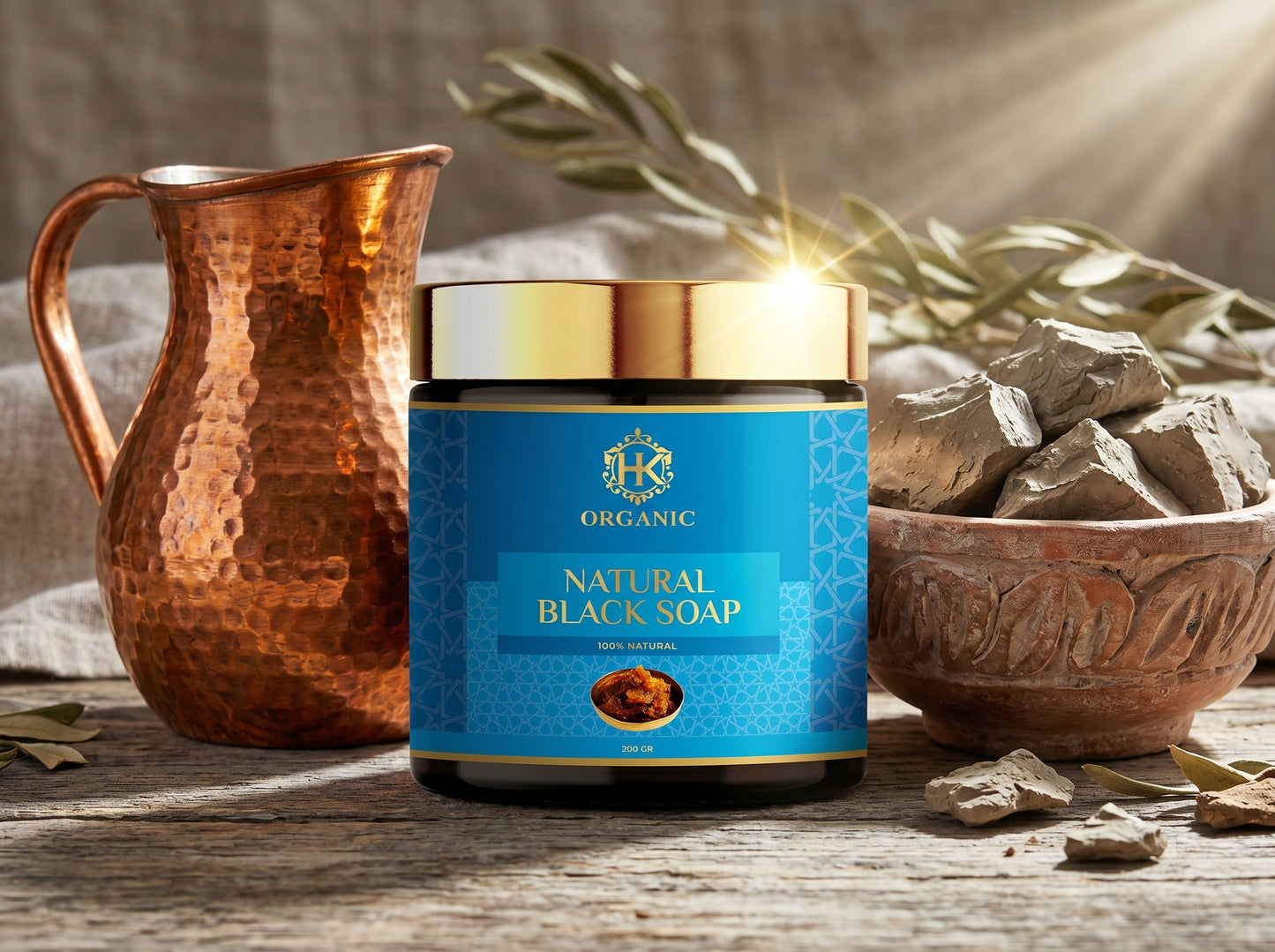 Jar of organic natural black soap with a rustic setting featuring a copper pitcher and bowl of soap.