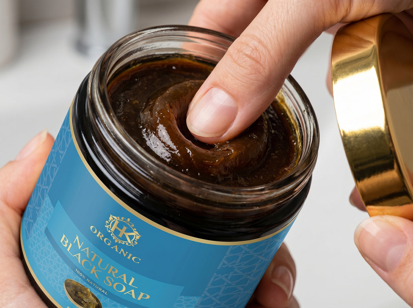 Jar of organic black soap with a hand holding the lid.