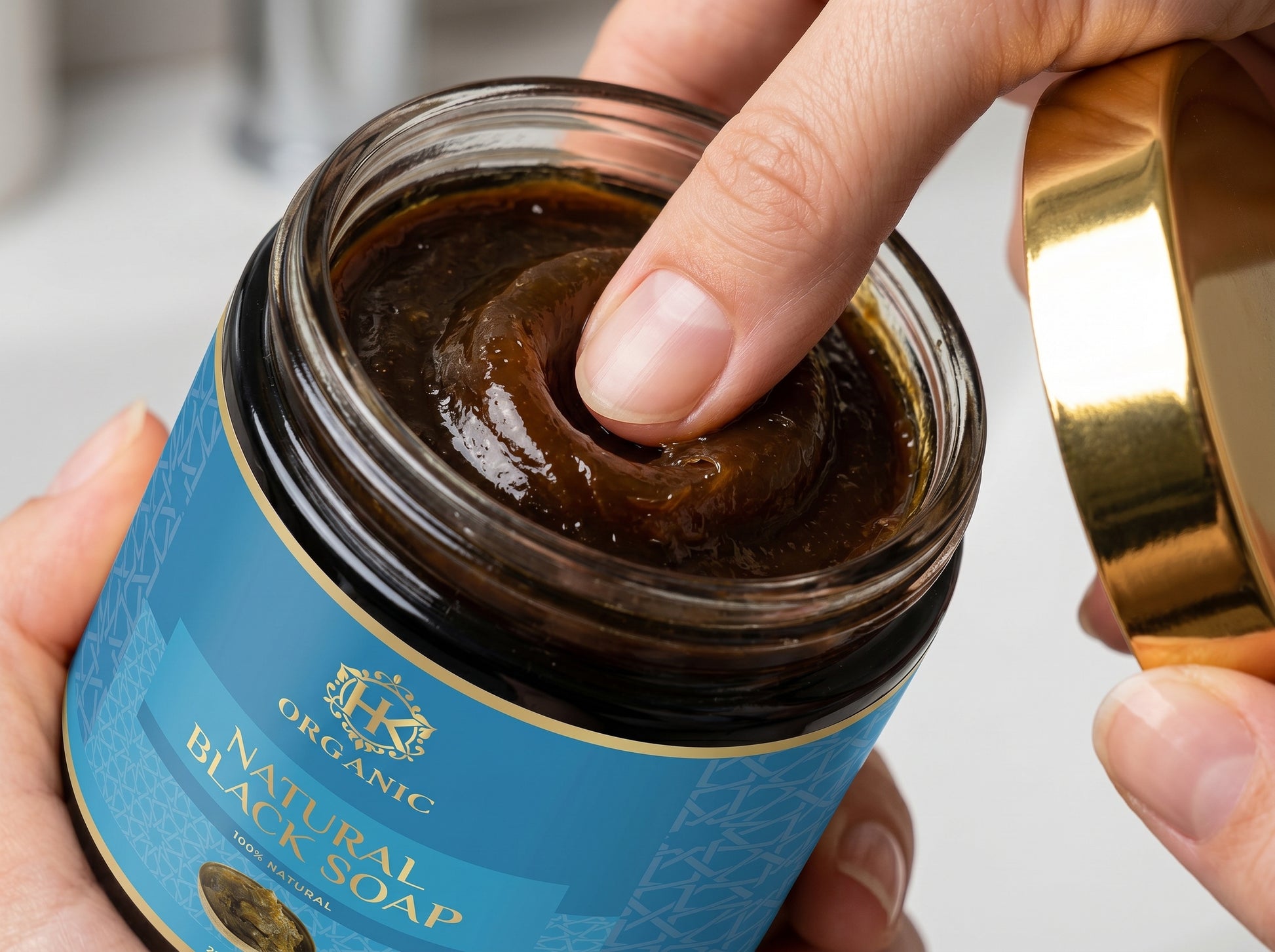 Jar of organic black soap with a hand holding the lid.
