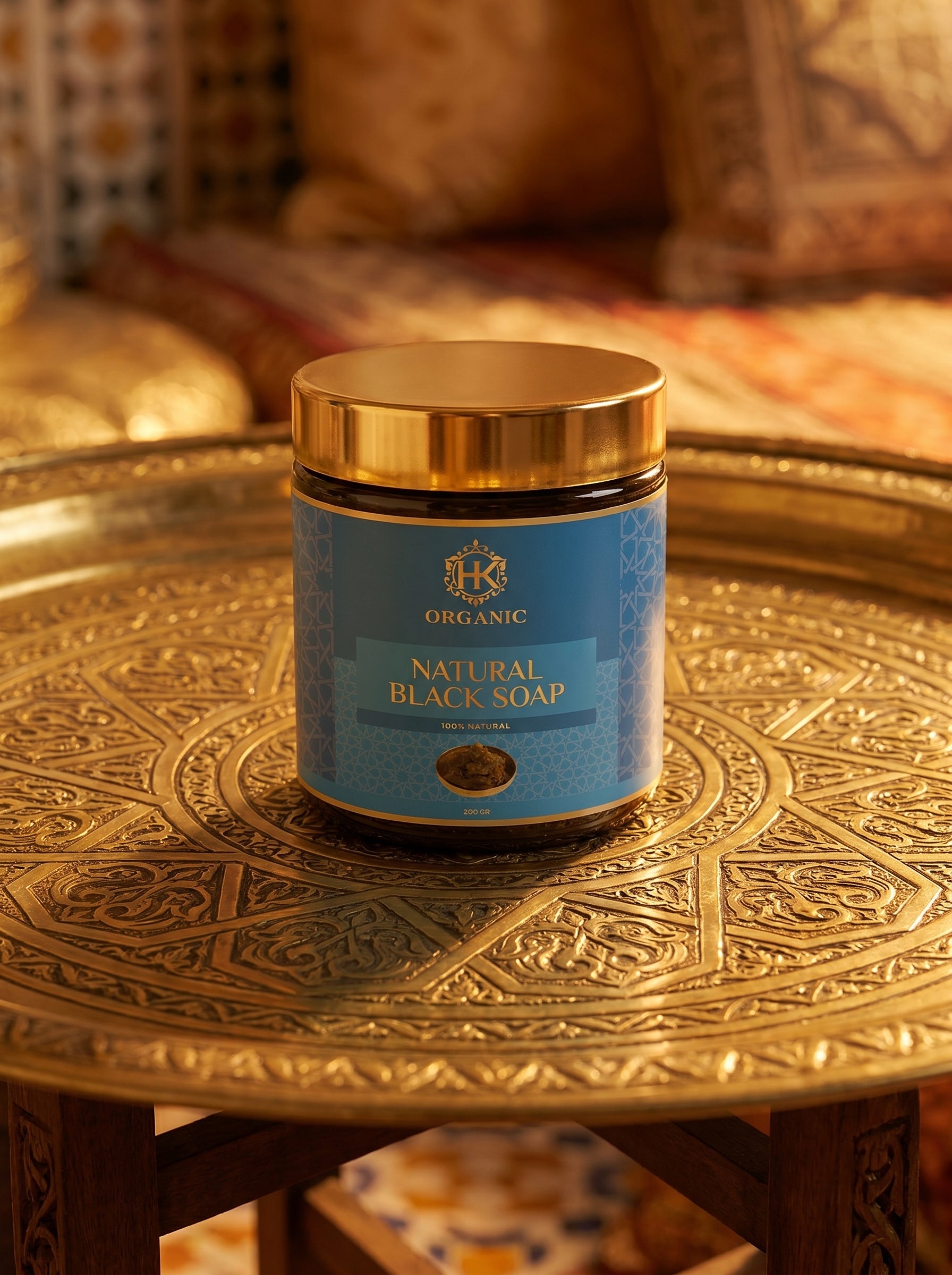 Jar of natural black soap on a decorative gold table with a blurred background