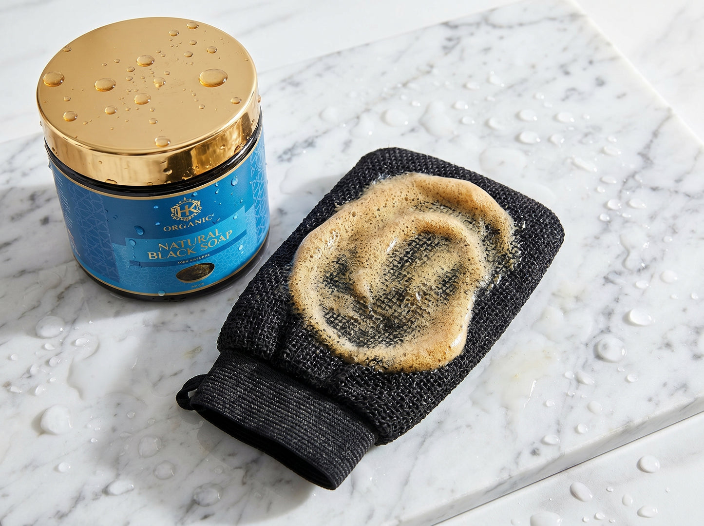 Blue jar with gold lid and black exfoliating glove on a marble surface