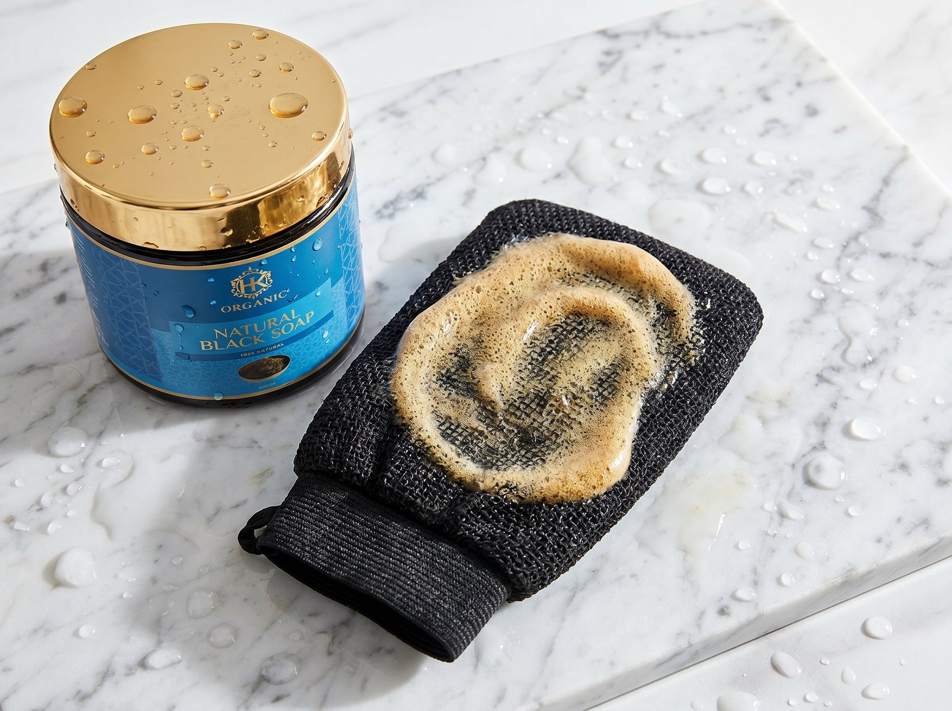 Blue jar with gold lid and black exfoliating glove on a marble surface