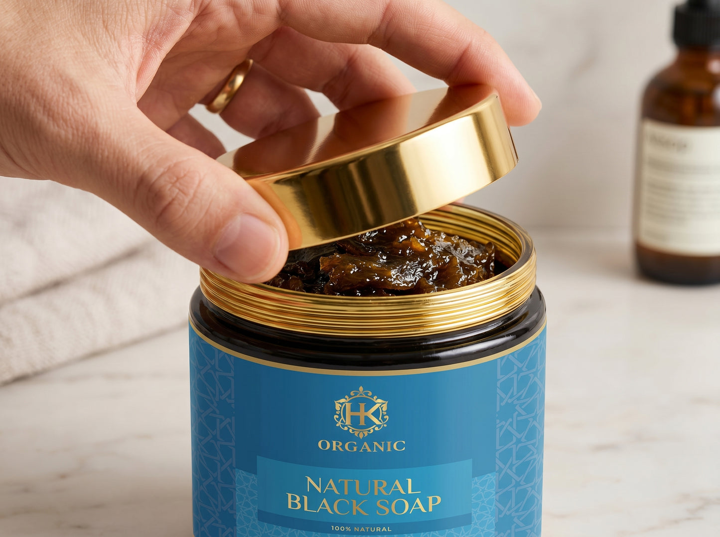 Hand opening a jar of organic natural black soap with a gold lid.