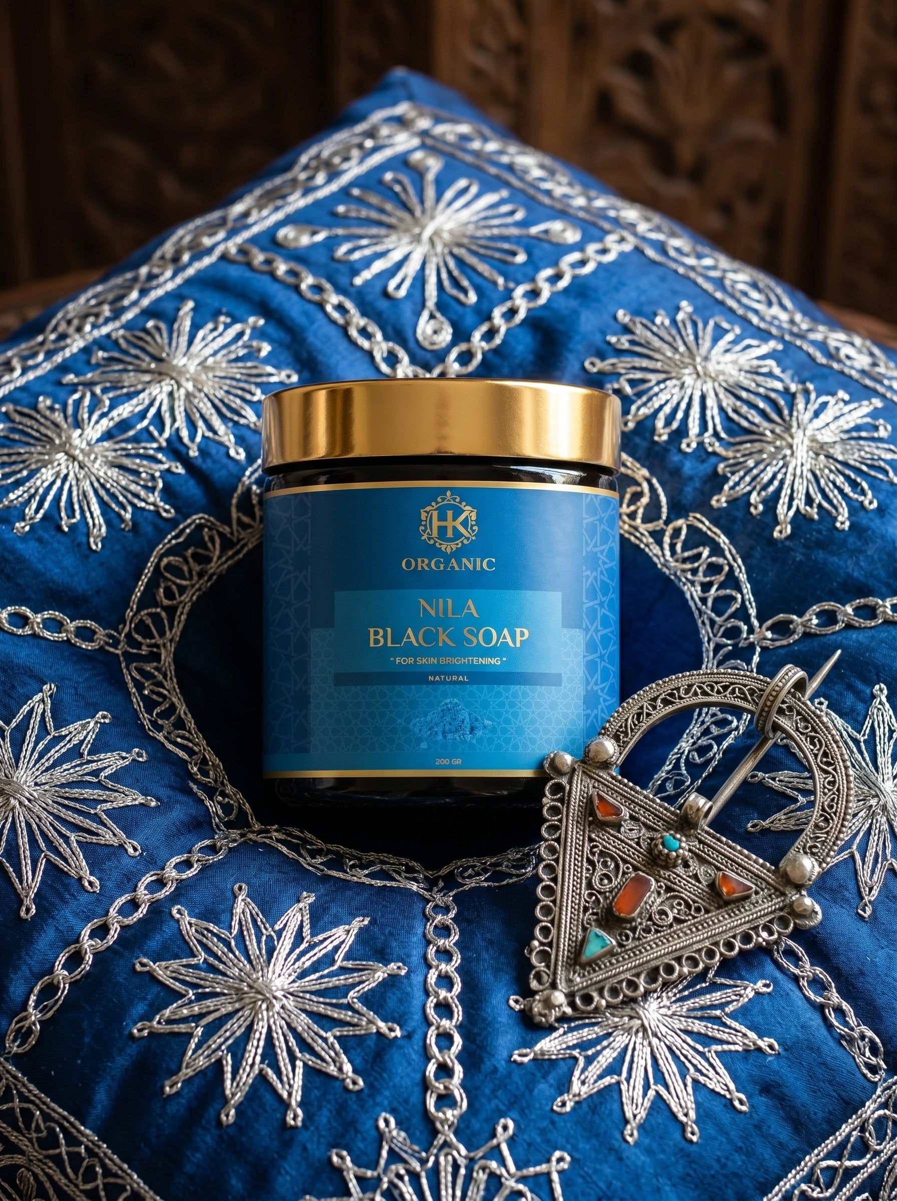 Blue container of Nila Black Soap on a decorative blue fabric background