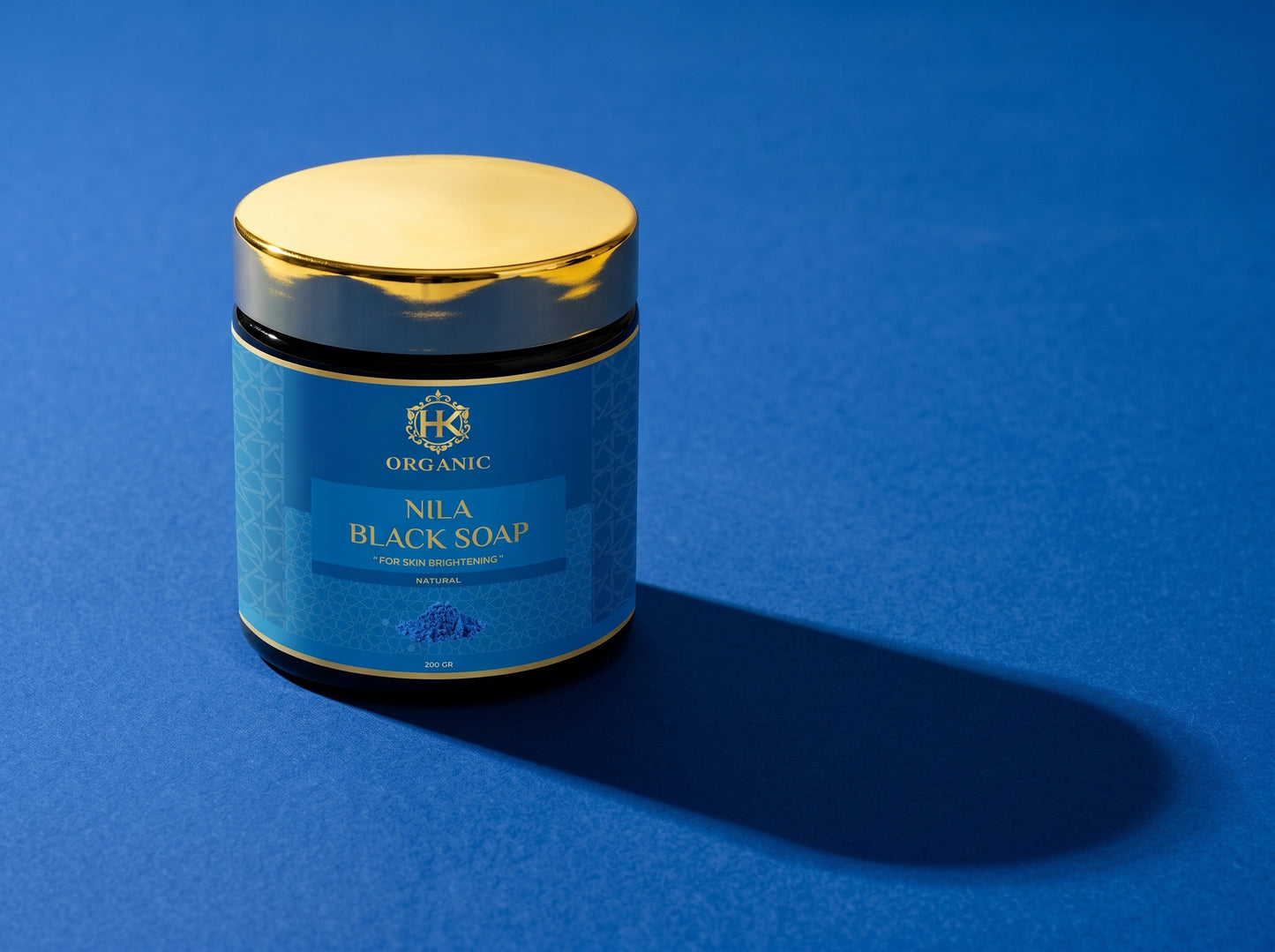Jar of Nila Black Soap with gold lid on a blue background