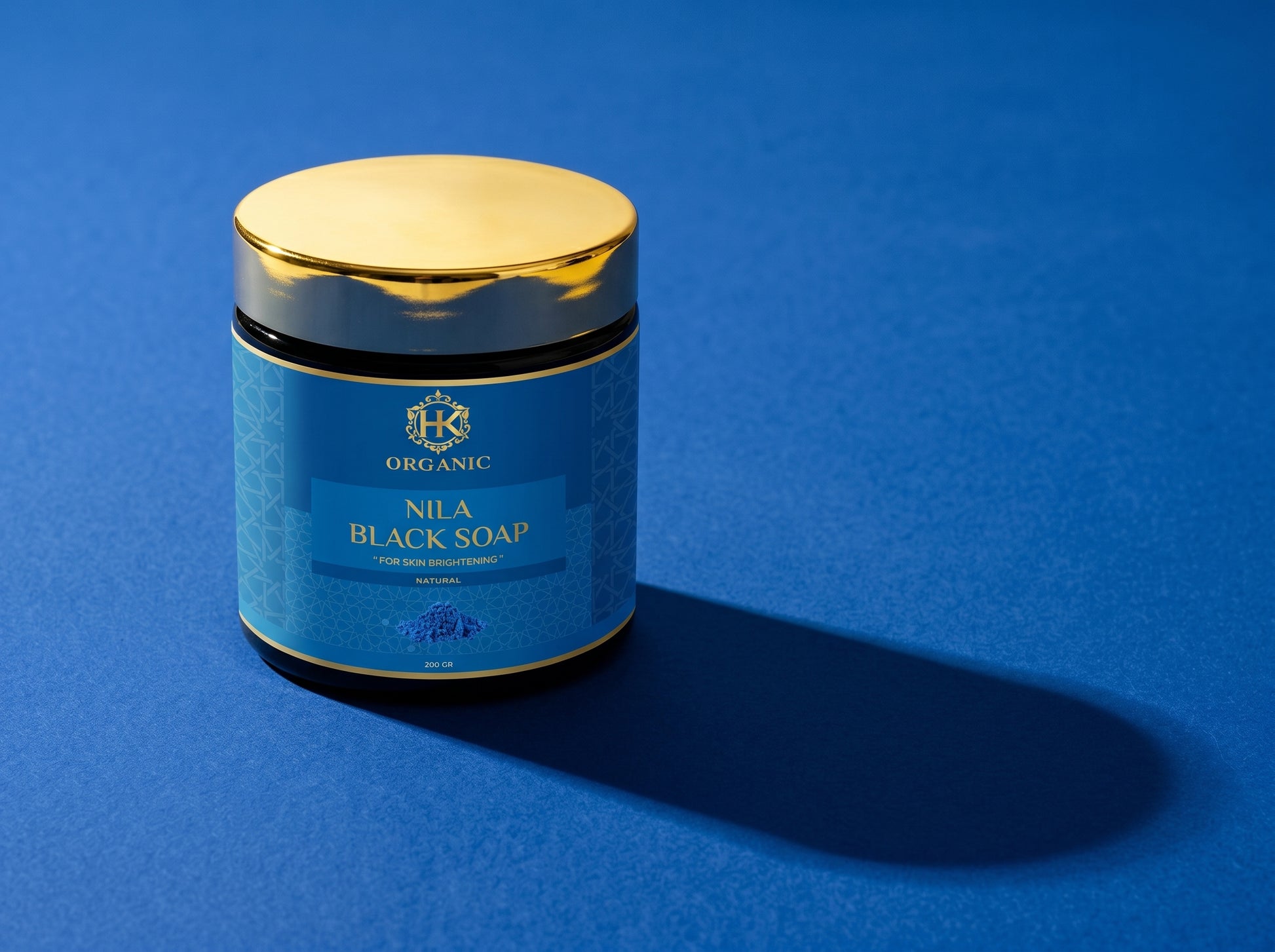 Jar of Nila Black Soap with gold lid on a blue background