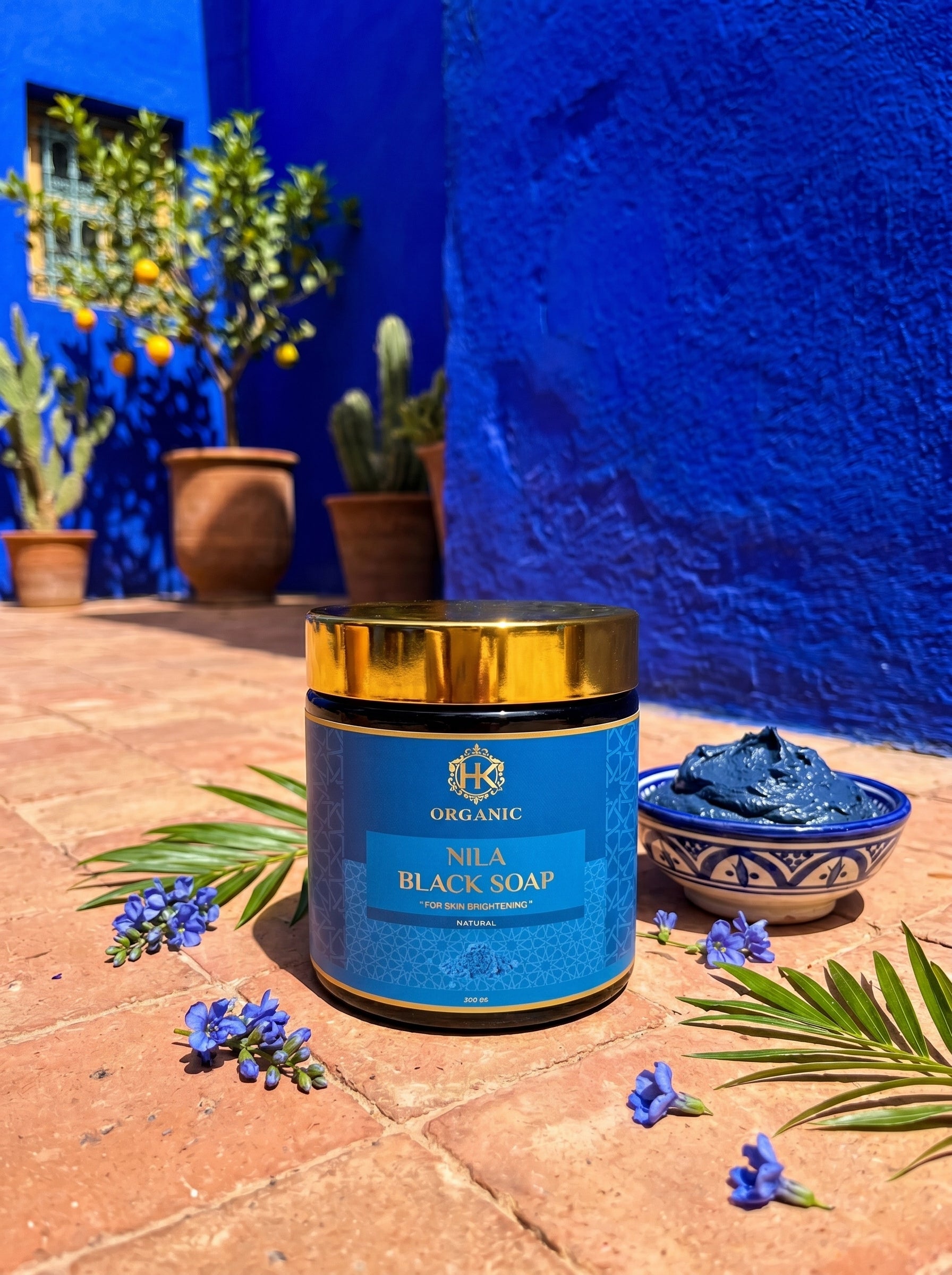 Blue jar of organic black soap with a blue wall and plants in the background