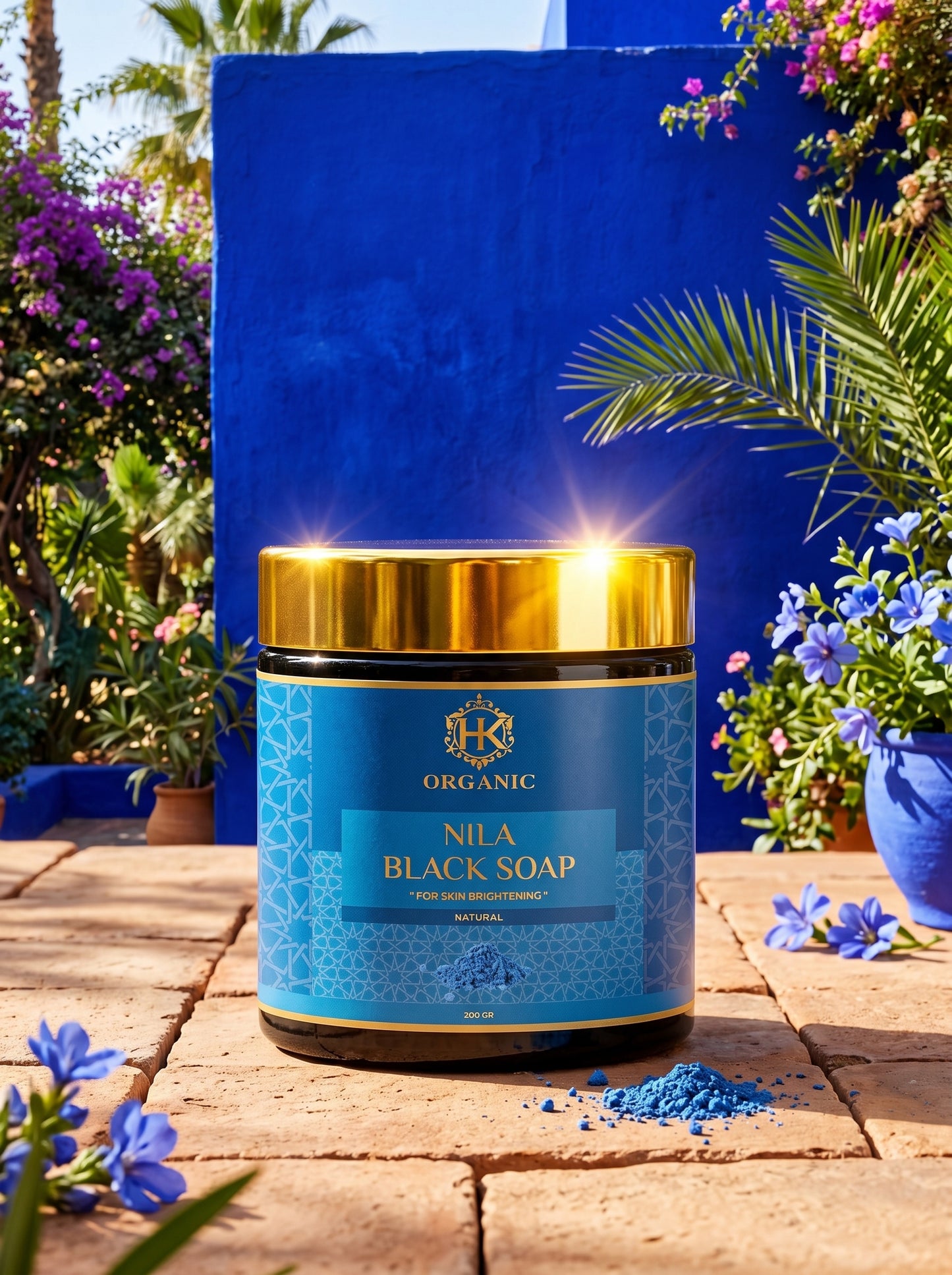 Nila Black Soap container with blue packaging and gold lid on a stone surface with flowers and plants in the background.