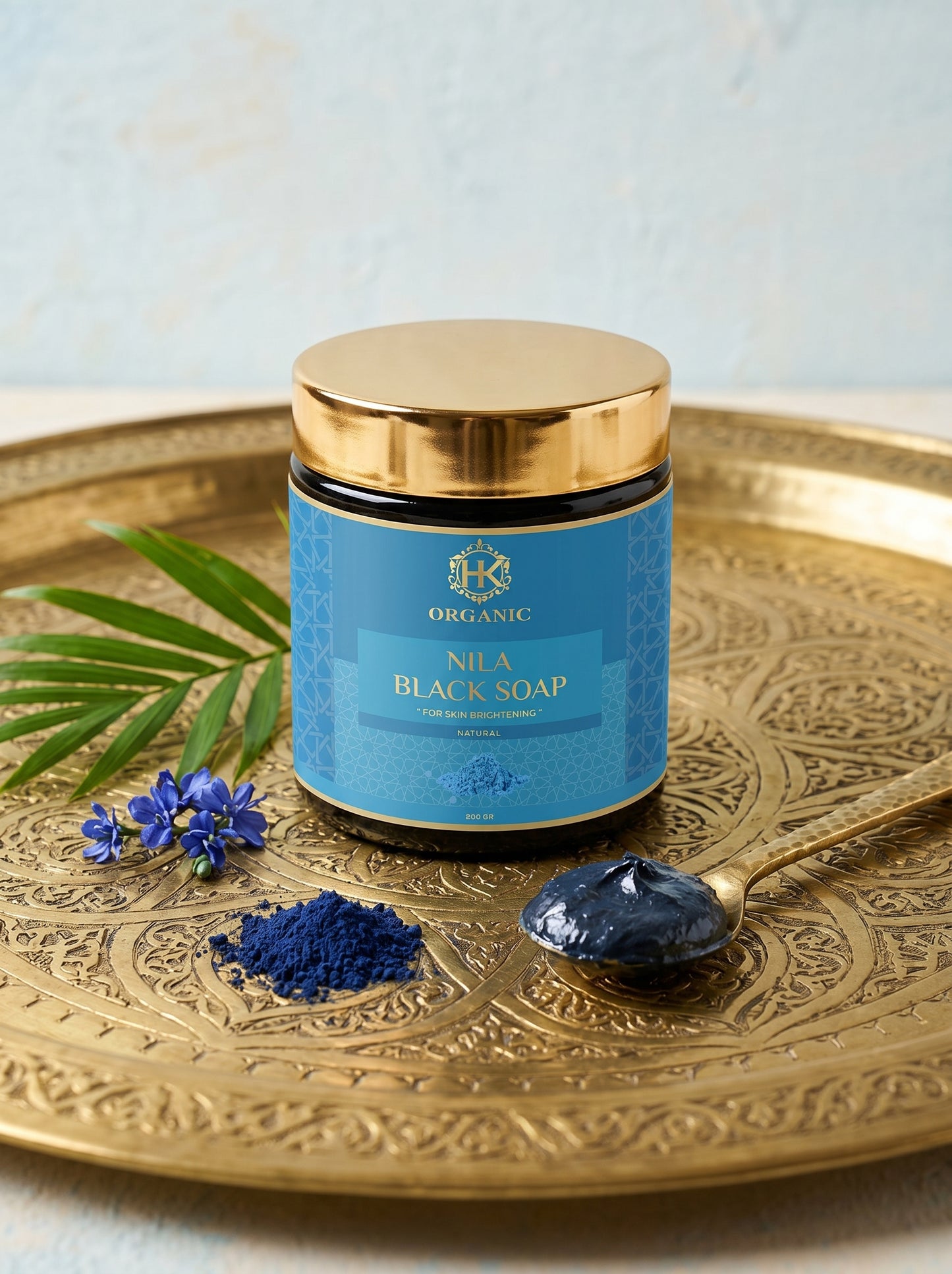 Jar of Nila Black Soap on a decorative gold tray with leaves and a spoonful of soap.