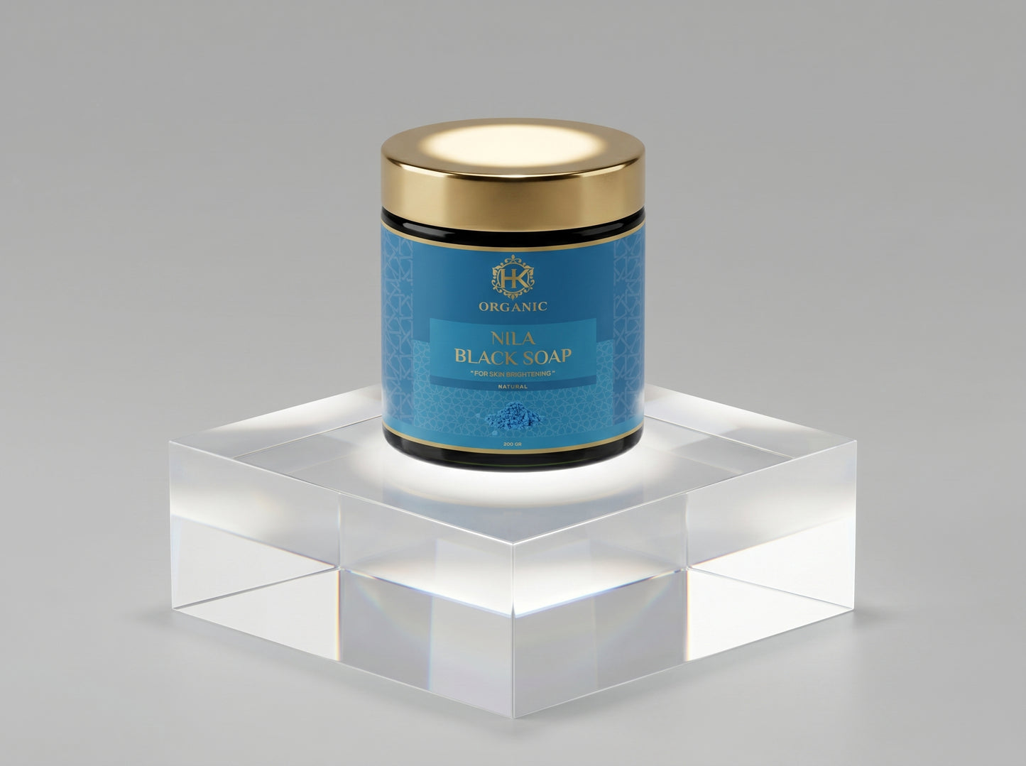 Jar of Nila Black Soap with gold lid on a clear stand against a gray background