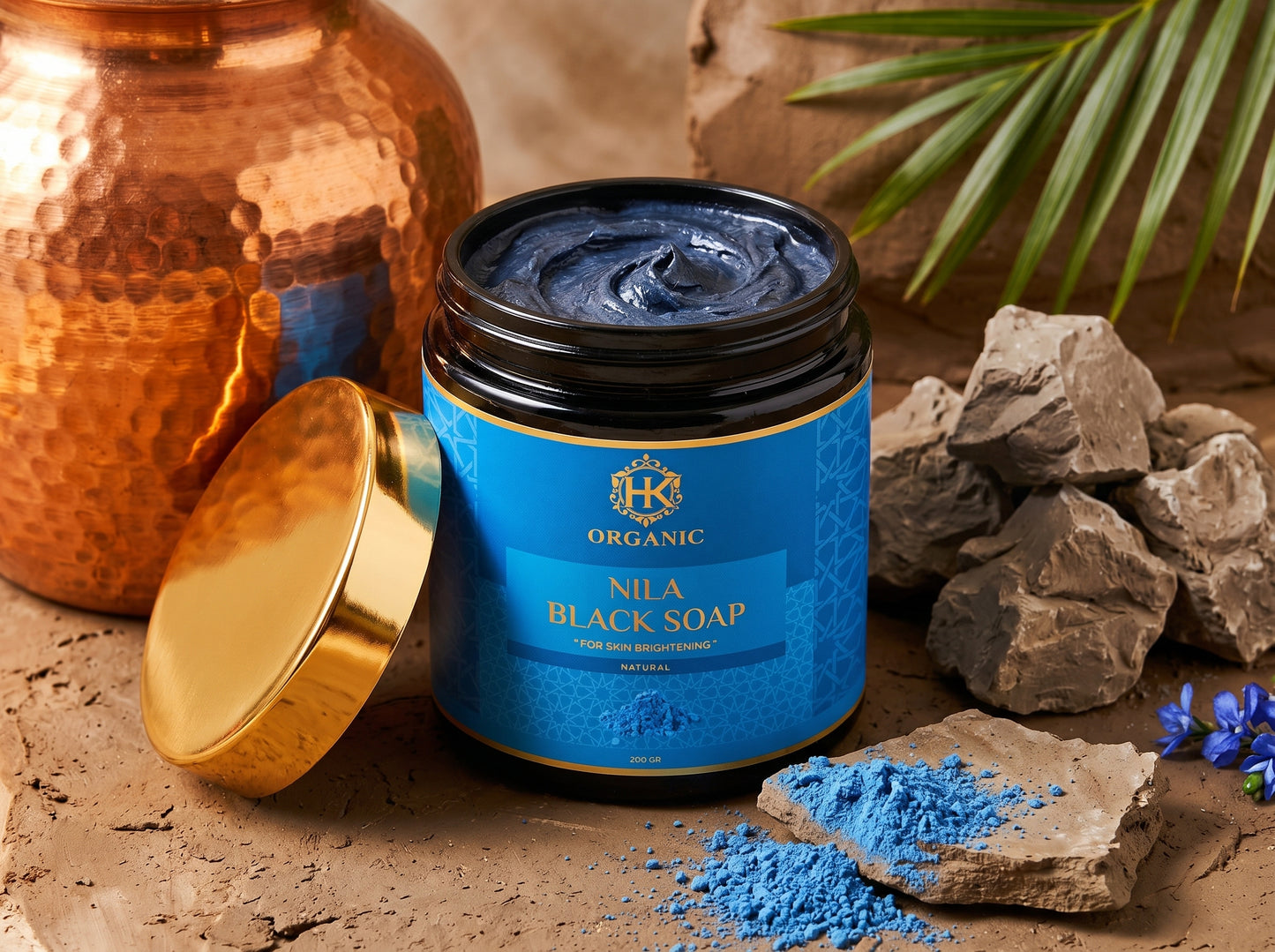 Jar of Nila Black Soap with gold lid on a textured surface with rocks and leaves.
