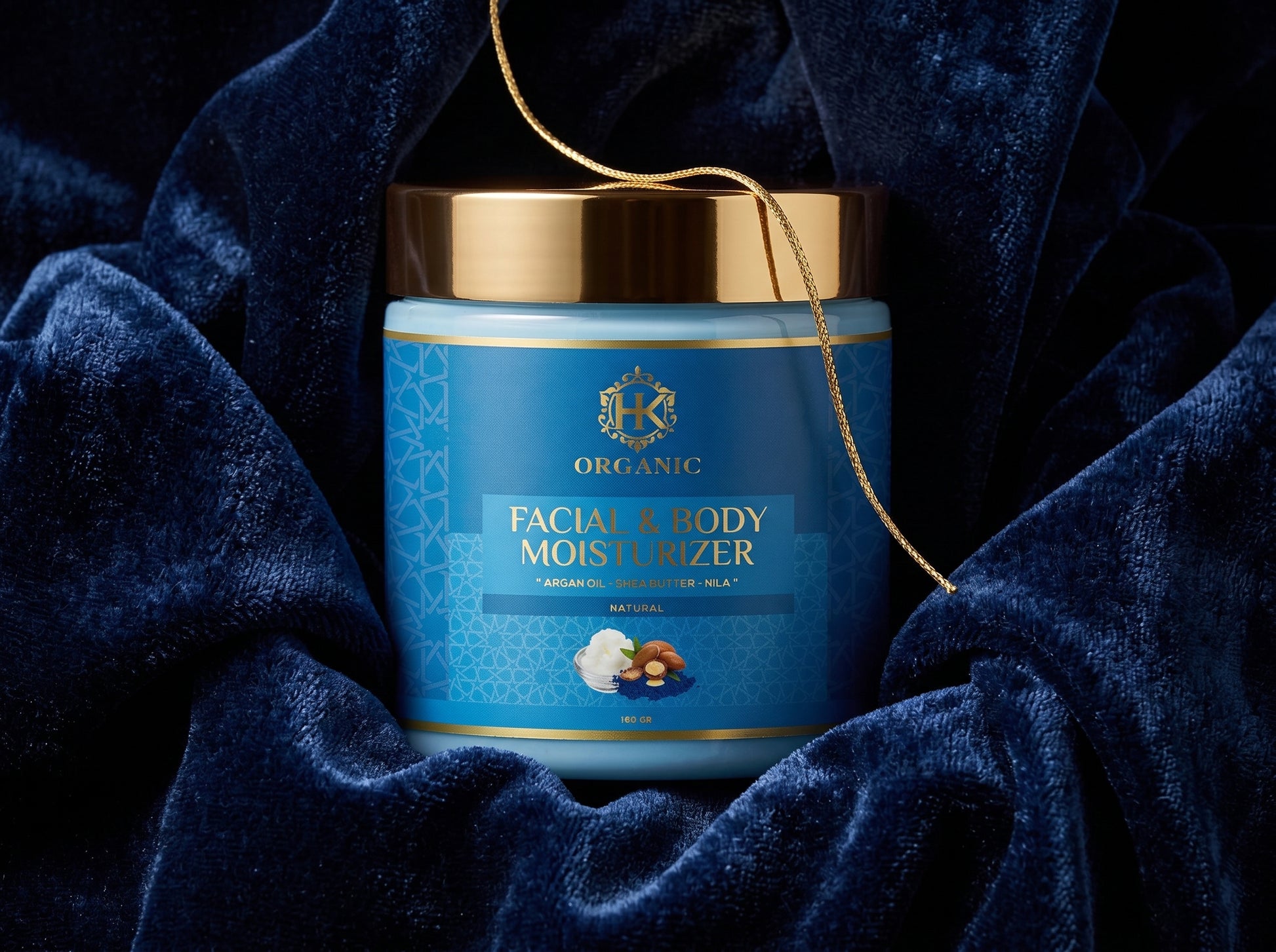 Blue jar of facial and body moisturizer with gold lid on a dark blue fabric background