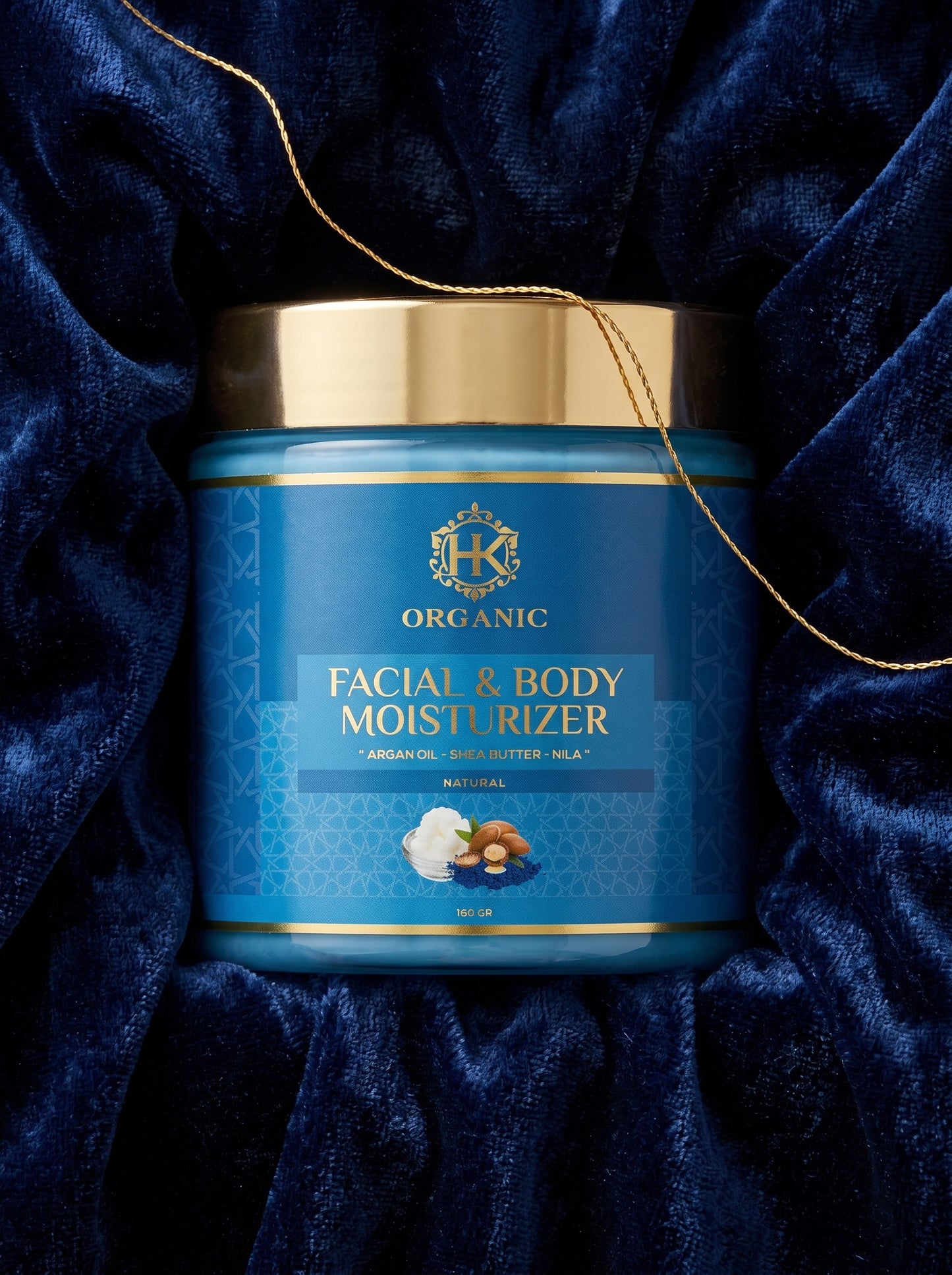Blue jar of facial and body moisturizer with gold lid on a blue velvet background