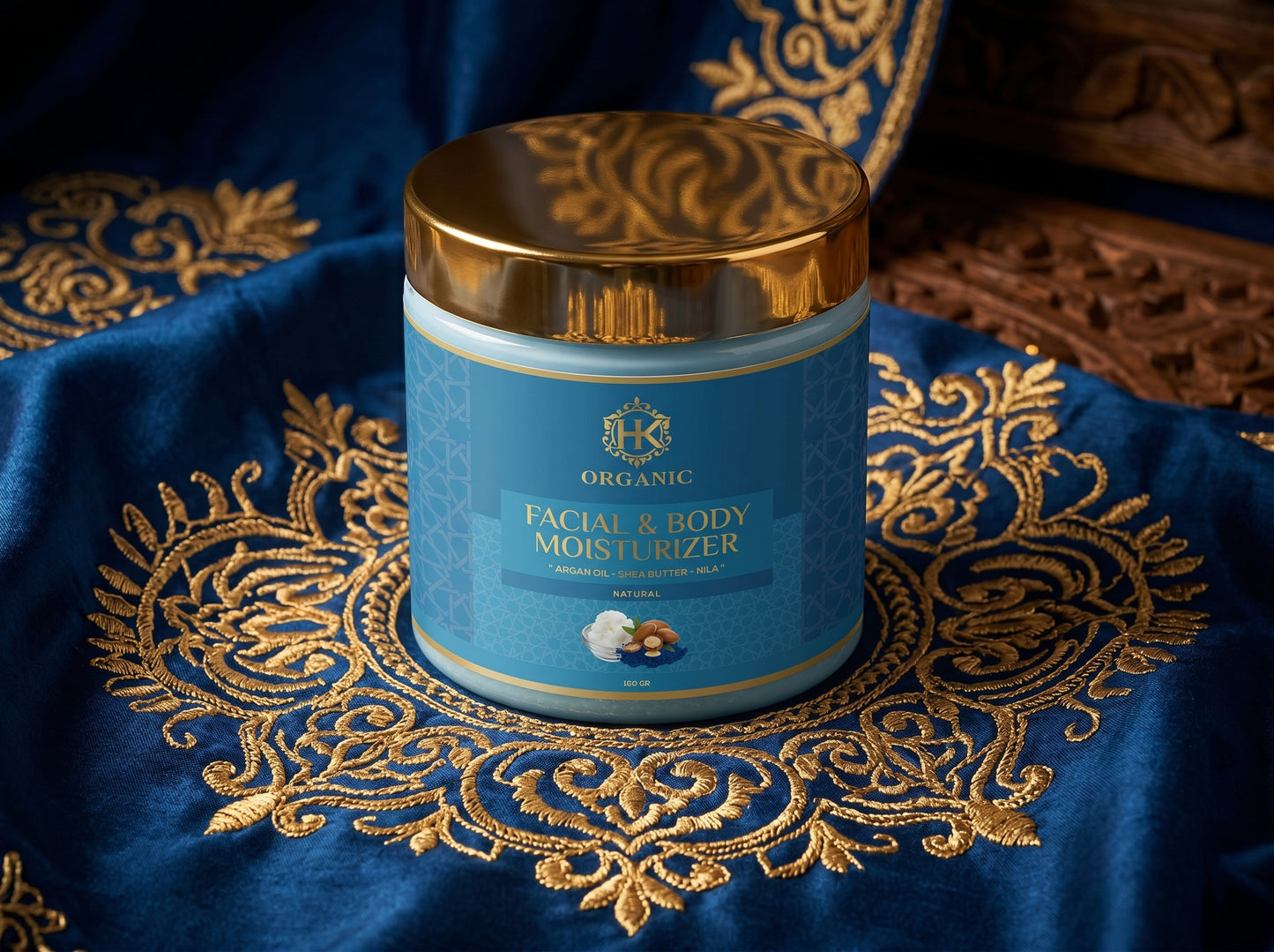 Facial and body moisturizer jar with gold lid on a decorative blue fabric background