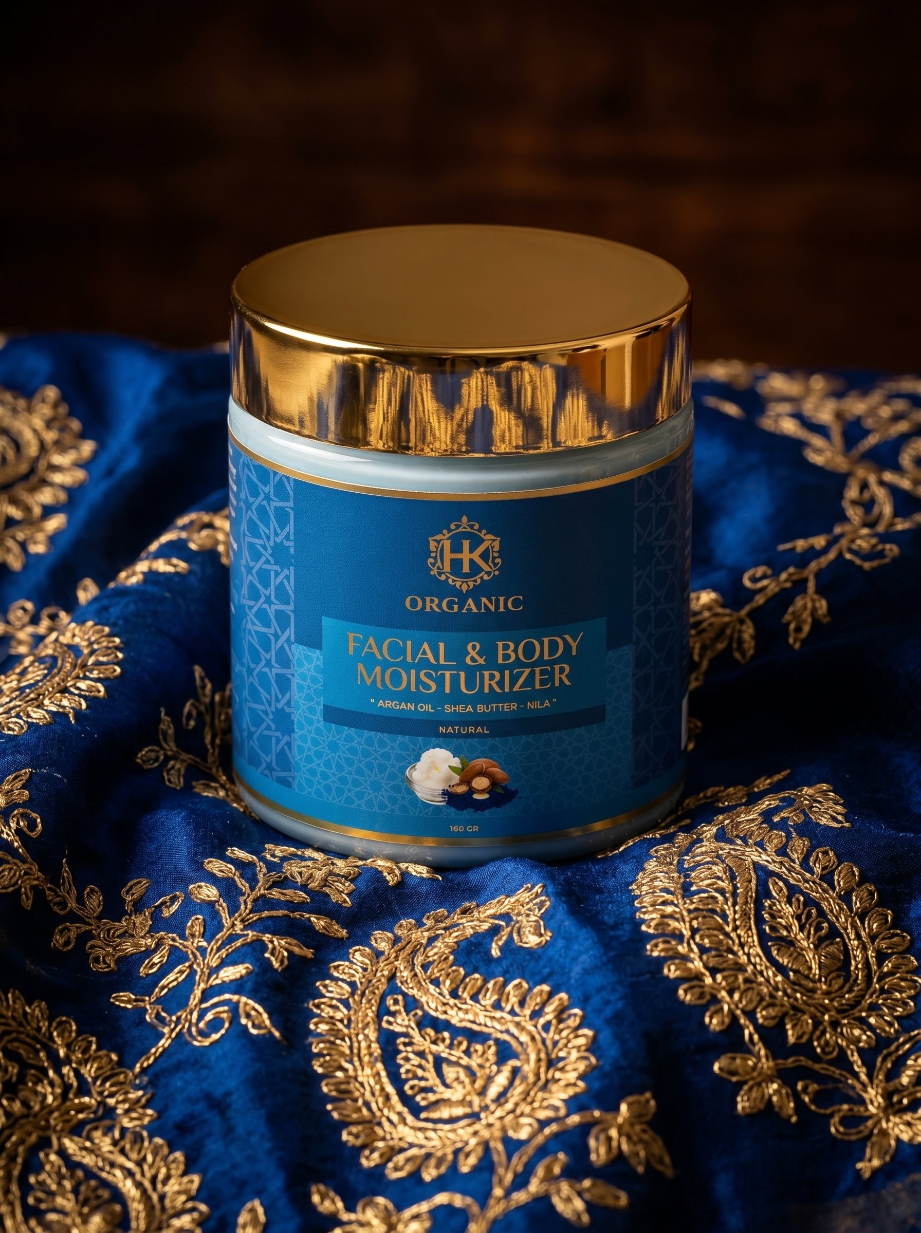 Facial and body moisturizer jar with gold lid on a blue fabric background