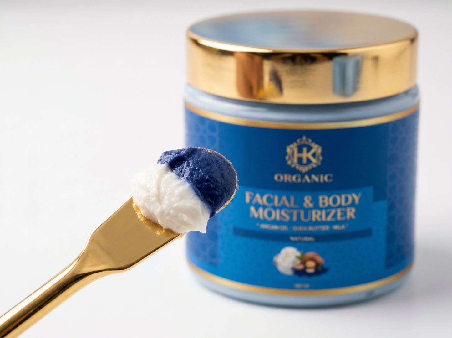 Blue jar of facial and body moisturizer with a gold lid and spoonful of cream on a white background