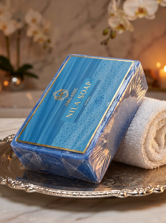 Blue Nila Soap packaging on a silver tray with a white towel and decorative flowers in the background.