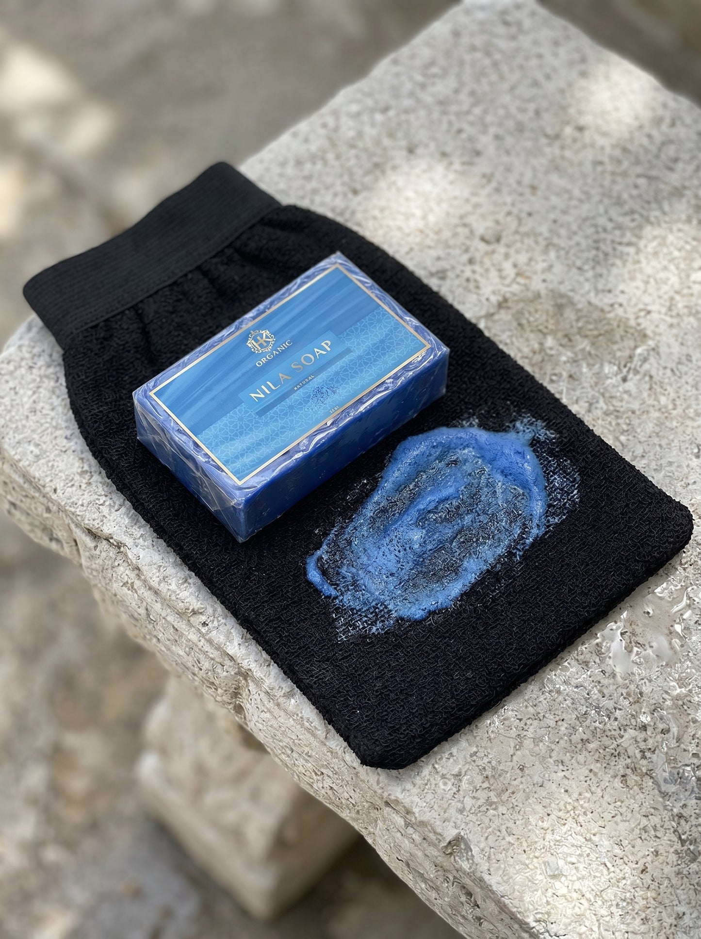 Bar of blue soap on a black washcloth with soap suds on a stone surface
