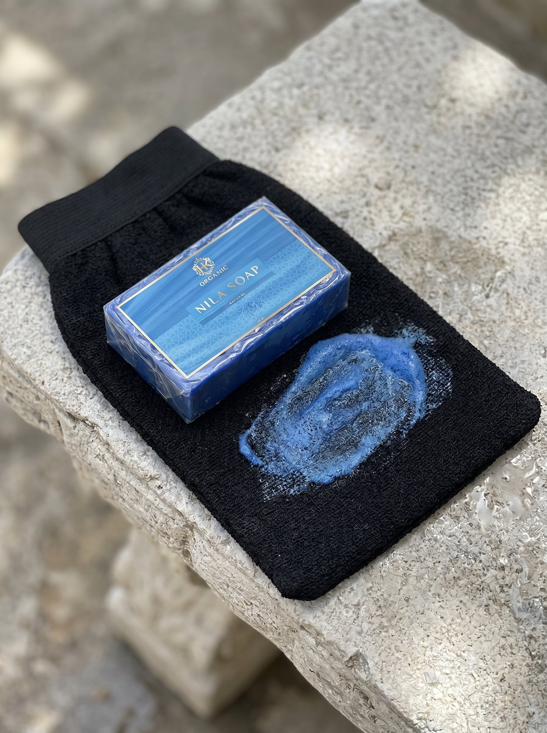 Bar of blue soap on a black washcloth with soap suds on a stone surface