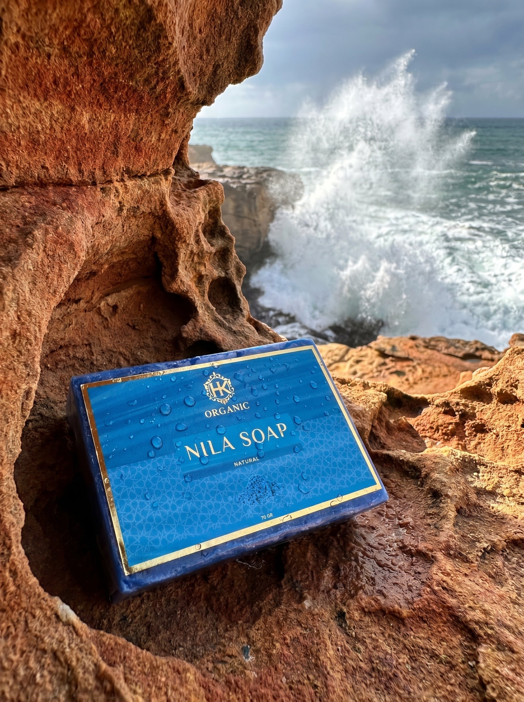 Nila Soap packaging on a rocky coastal background with ocean waves.