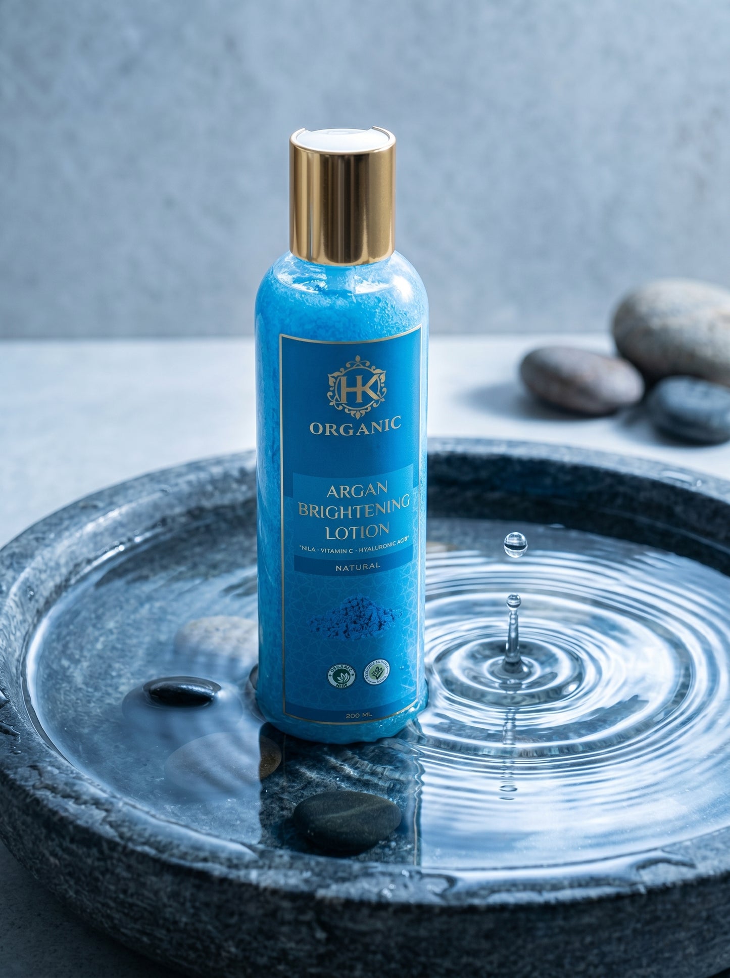 Blue bottle of argan brightening lotion on a stone surface with water droplets.