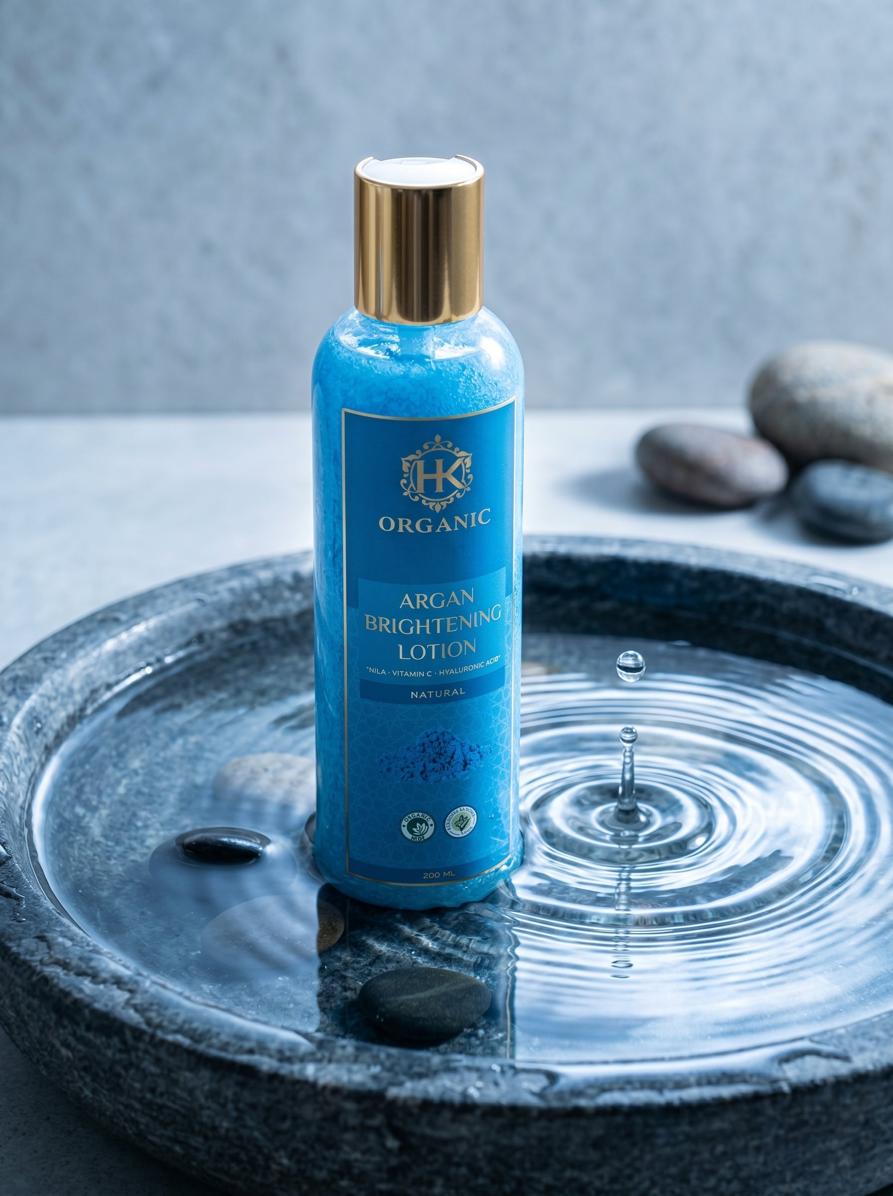 Blue bottle of argan brightening lotion on a stone surface with water droplets.