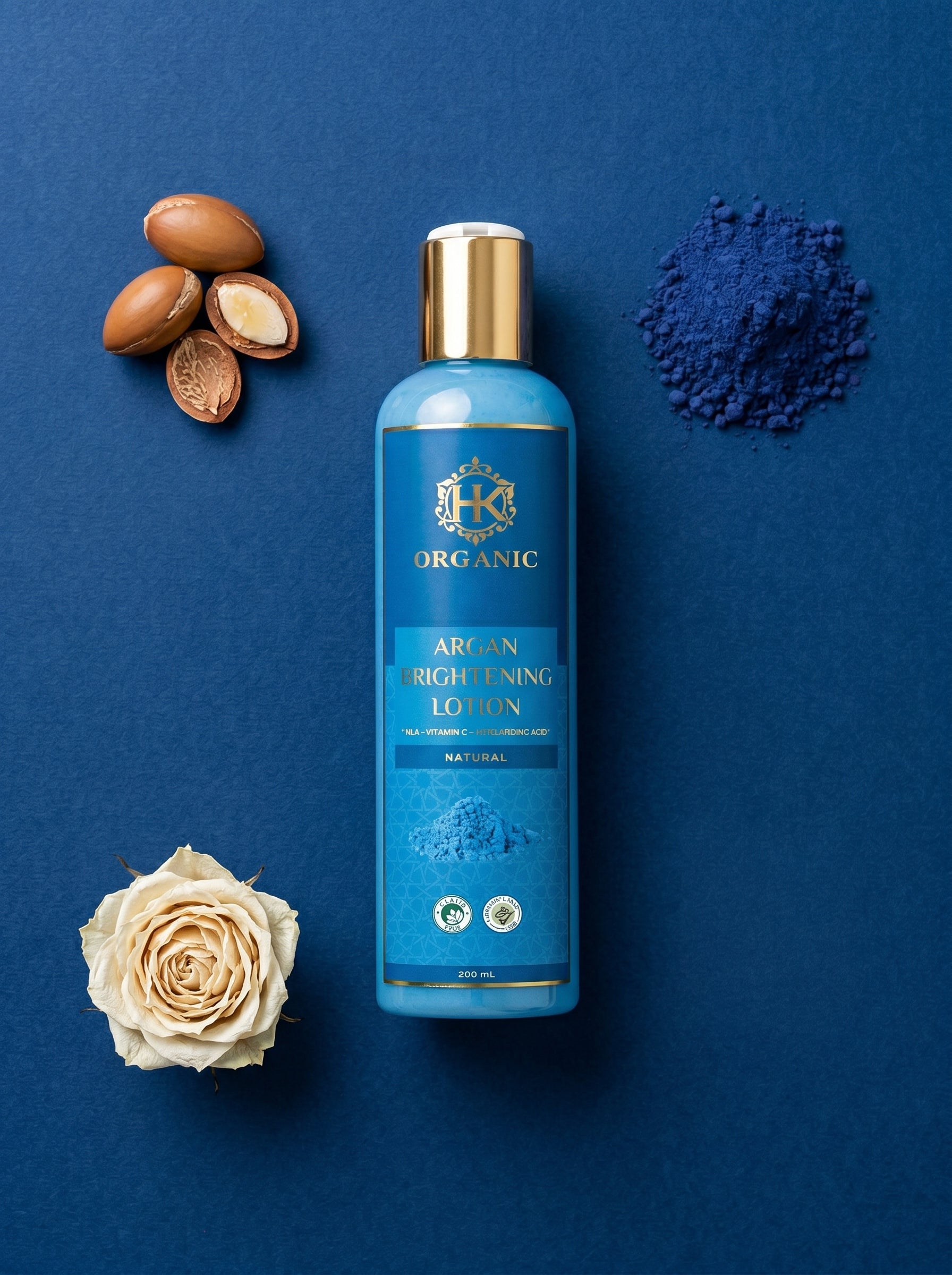 Blue bottle of organic argan oil lotion on a blue background with argan seeds, rose, and blue powder.