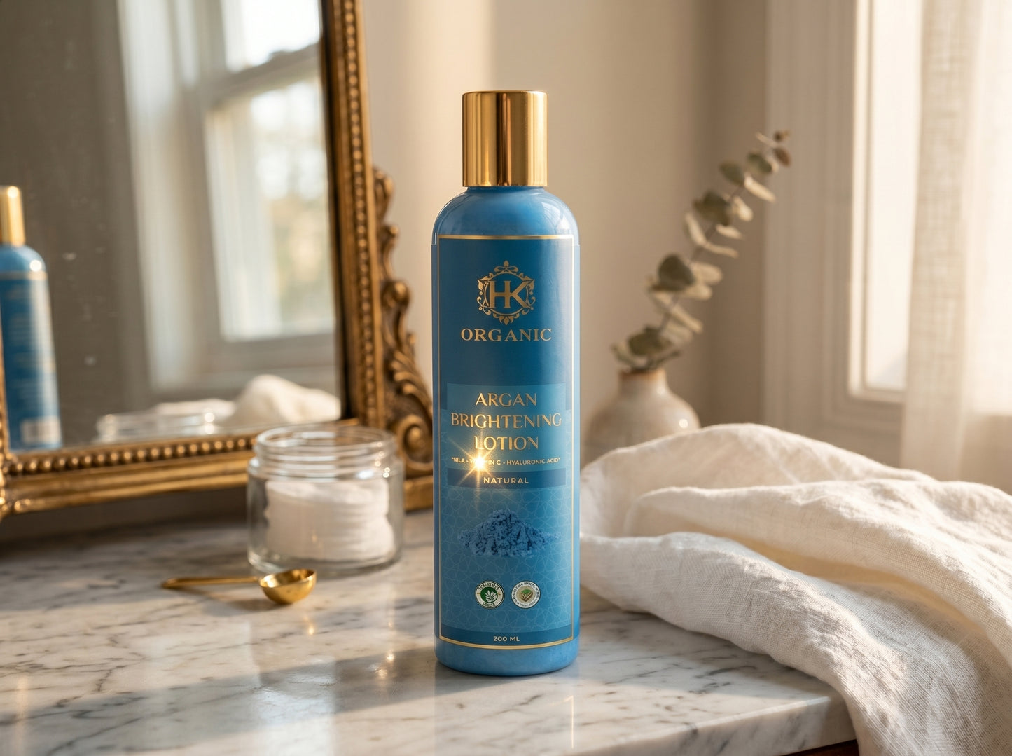 Blue bottle of K Organics Argan Brightening Lotion on a marble surface with decorative items in the background.