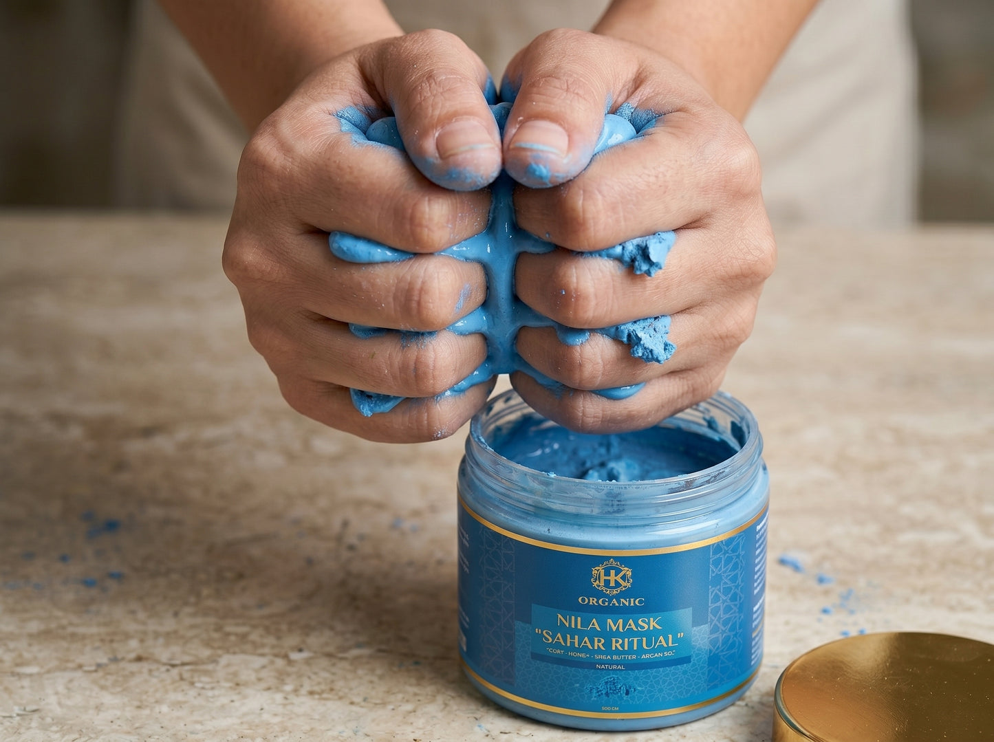 Person kneading blue clay mask from a jar labeled 'Nila Mask' on a wooden surface.