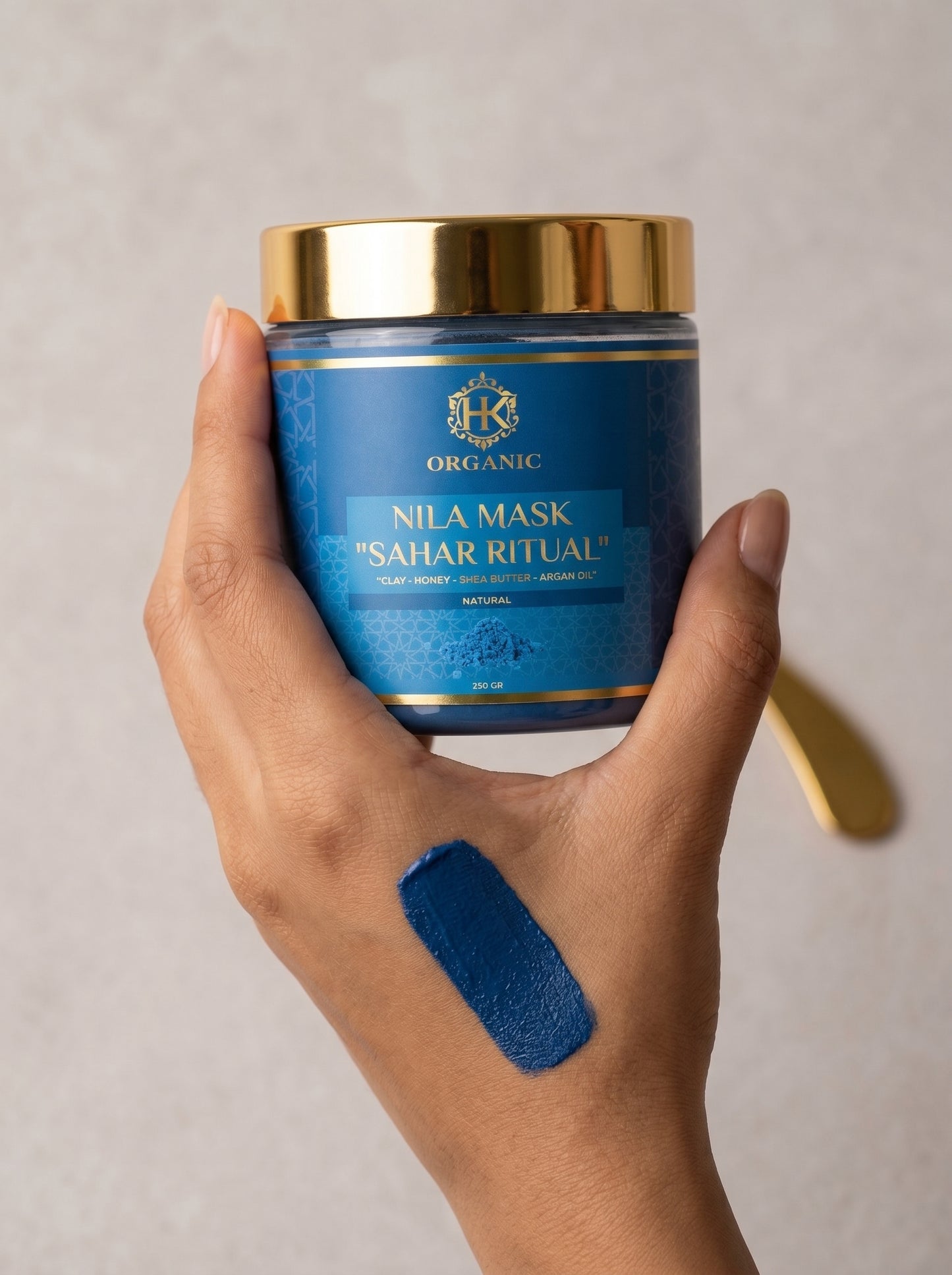 Hand holding a blue jar of Nila Mask with a gold lid against a neutral background