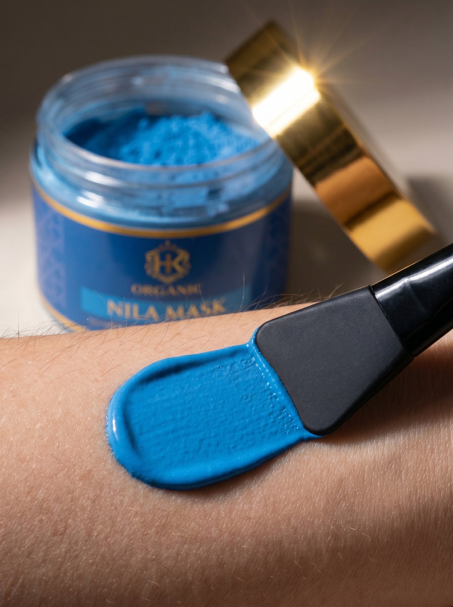 Blue mask on a person's arm with a jar and applicator in the background